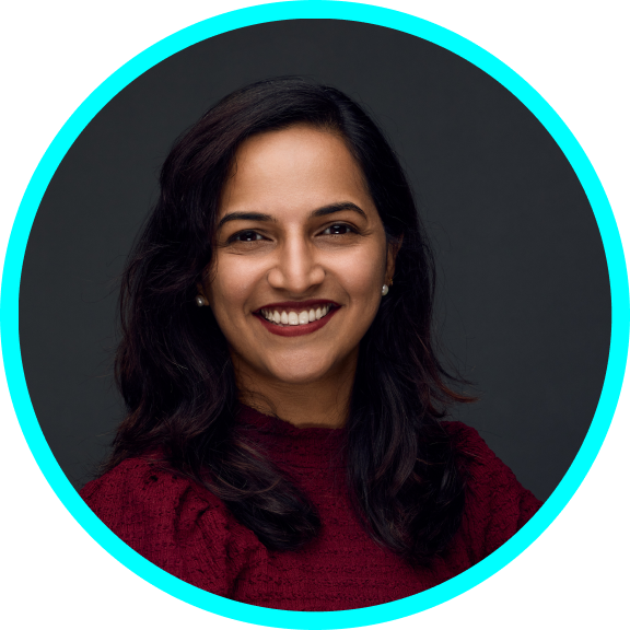 Ramya is a middle-aged Indian woman with brown complexion, shoulder height black hair and black eyes. She is wearing a red top, sitting diagonally and smiling at the camera.
