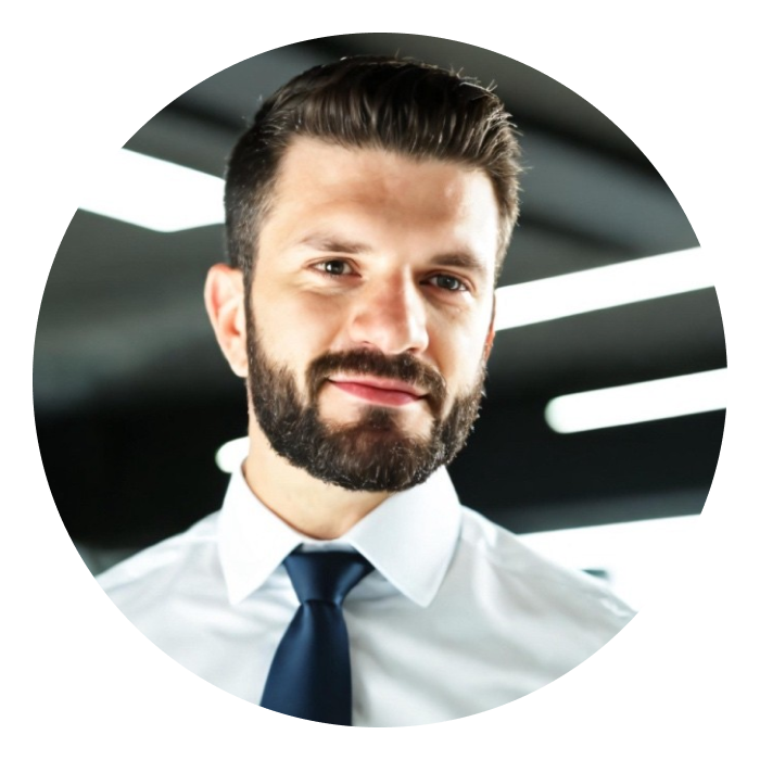Headshot of Tom - Tom has light skin, dark hair and beard, and is wearing a white formal shirt with a navy tie. 