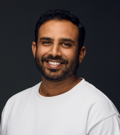 Dipin is a middle-aged Indian male with short dark hair and a beard. He is wearing a white t-shirt and smiling at the camera.
