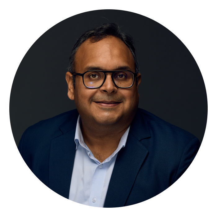 Headshot of Deep - an Indian man wearing glasses and a navy suit, smiling at the camera.