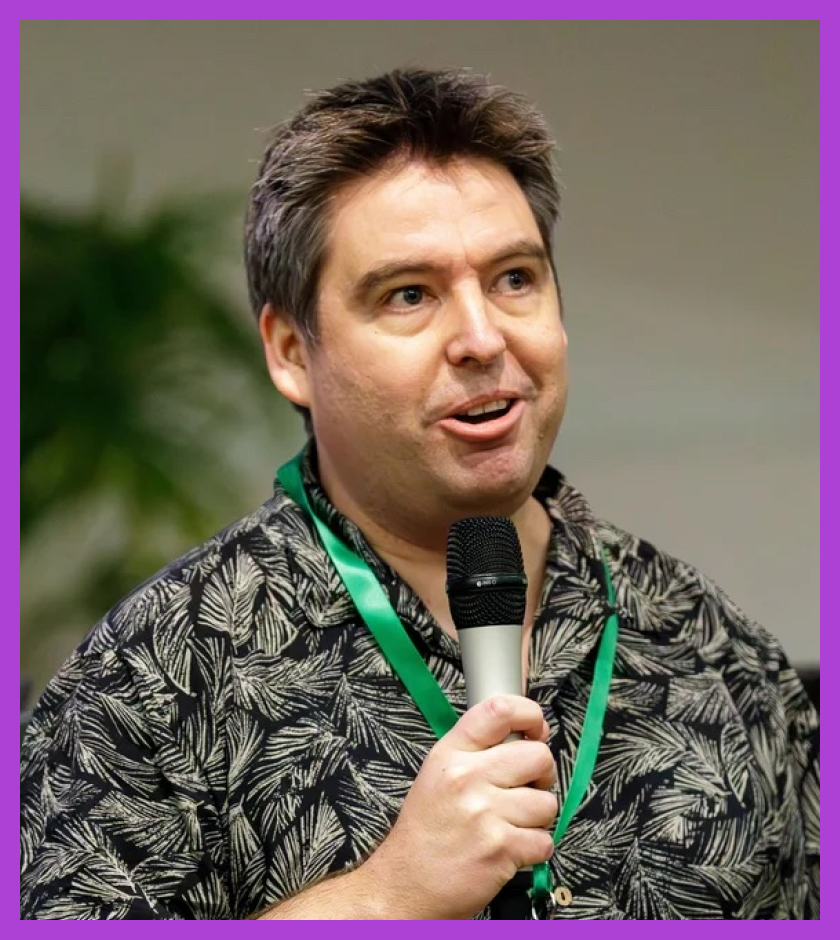 Aaron is a middle-aged white male, with dark brown hair. He is wearing a green floral shirt. 