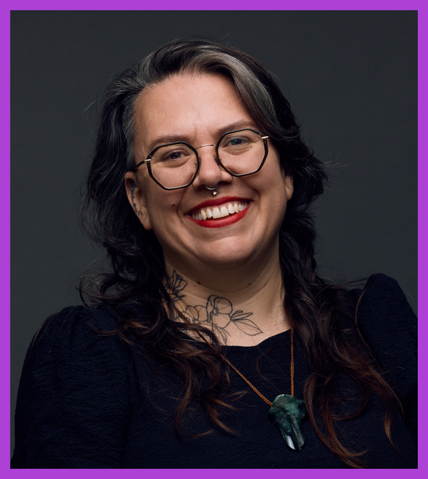 Headshot of Tamara, who has long brown hair, glasses, a big smile and has two full sleeve arm tattoos.