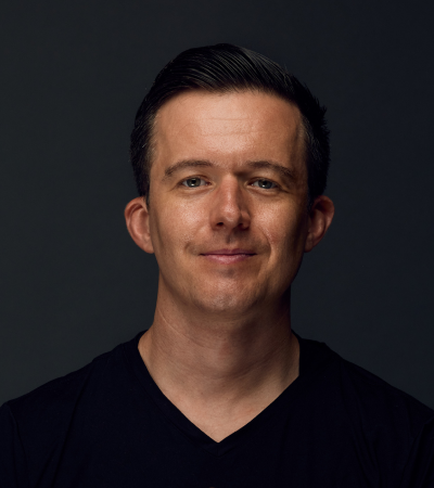 Oli is a Caucasian man with short brown hair, wearing a black t-shirt and smiling at the camera.