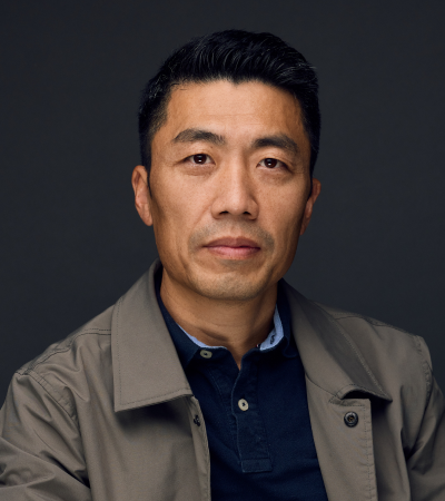 Feilong is a middle-aged Chinese man, wearing a navy blue shirt and smiling at the camera.
