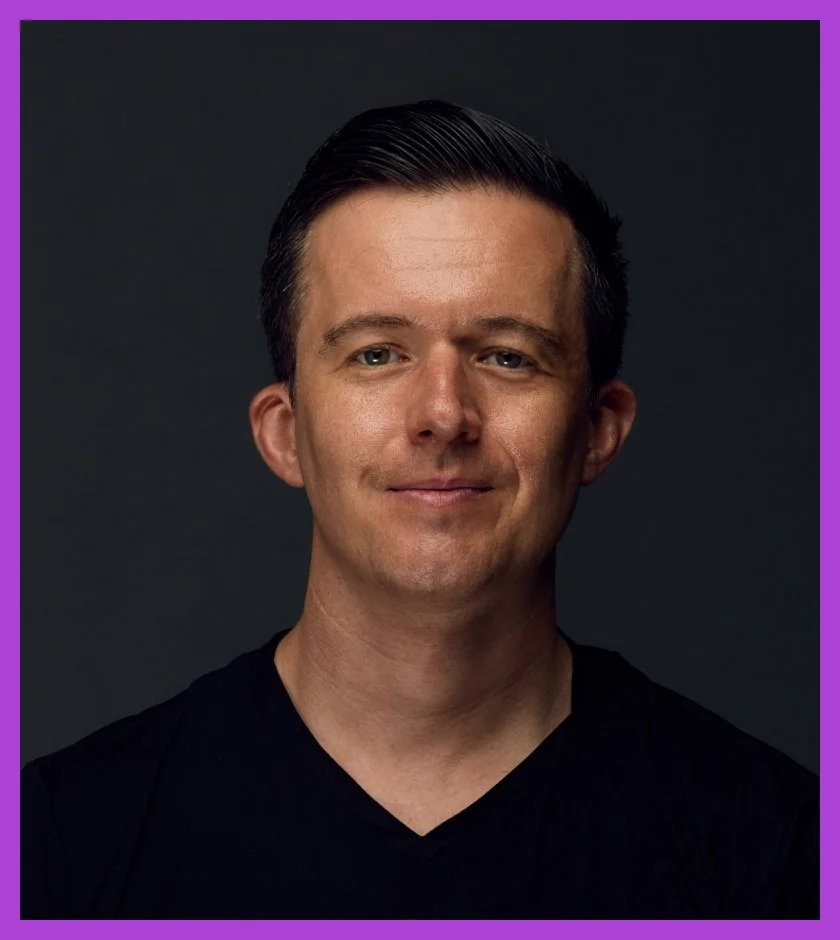 Oli is a Caucasian man with short brown hair, wearing a black t-shirt and smiling at the camera.