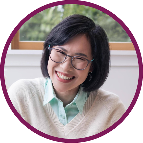 Prae is a middle-aged Thai woman with dark brown eyes and dark hair. She is wearing a white jumper and glasses, and smiling at the camera.