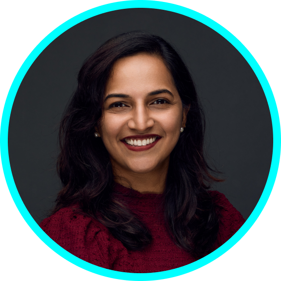 Ramya is a middle-aged Indian woman with brown complexion, shoulder height black hair and black eyes. She is wearing a red top, sitting diagonally and smiling at the camera.