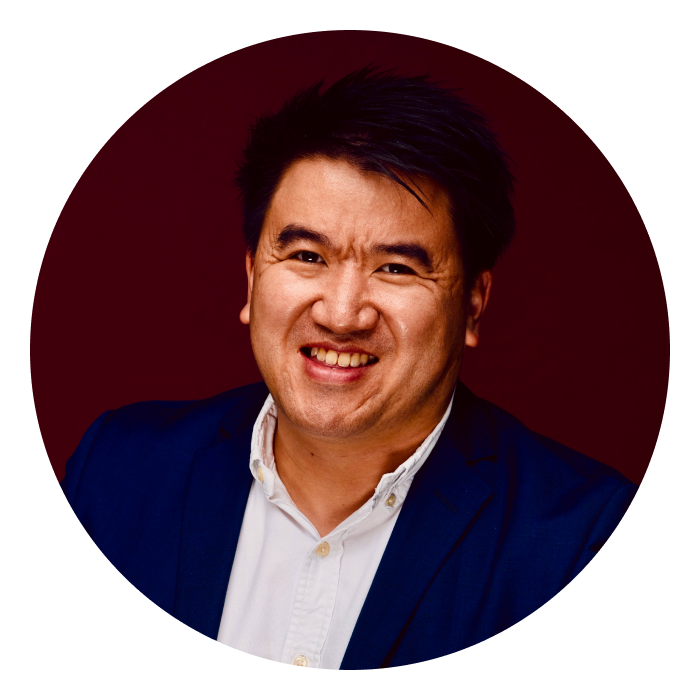 Greg is an Asian male who is smiling, wearing a blue blazer over a white collar shirt.