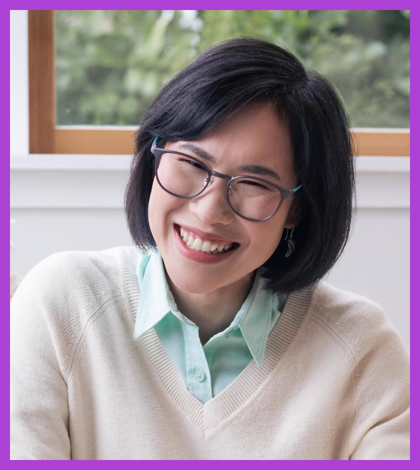 Prae is a middle-aged Thai woman with dark brown eyes and dark hair. She is wearing a white jumper and glasses, and smiling at the camera.