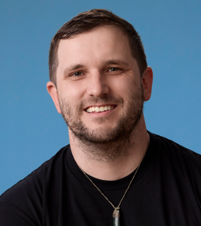 Headshot of Peter - a man in his mid-30’s with short brown hair and stubble wearing a pounamu, and a black shirt with a PrivSec logo.