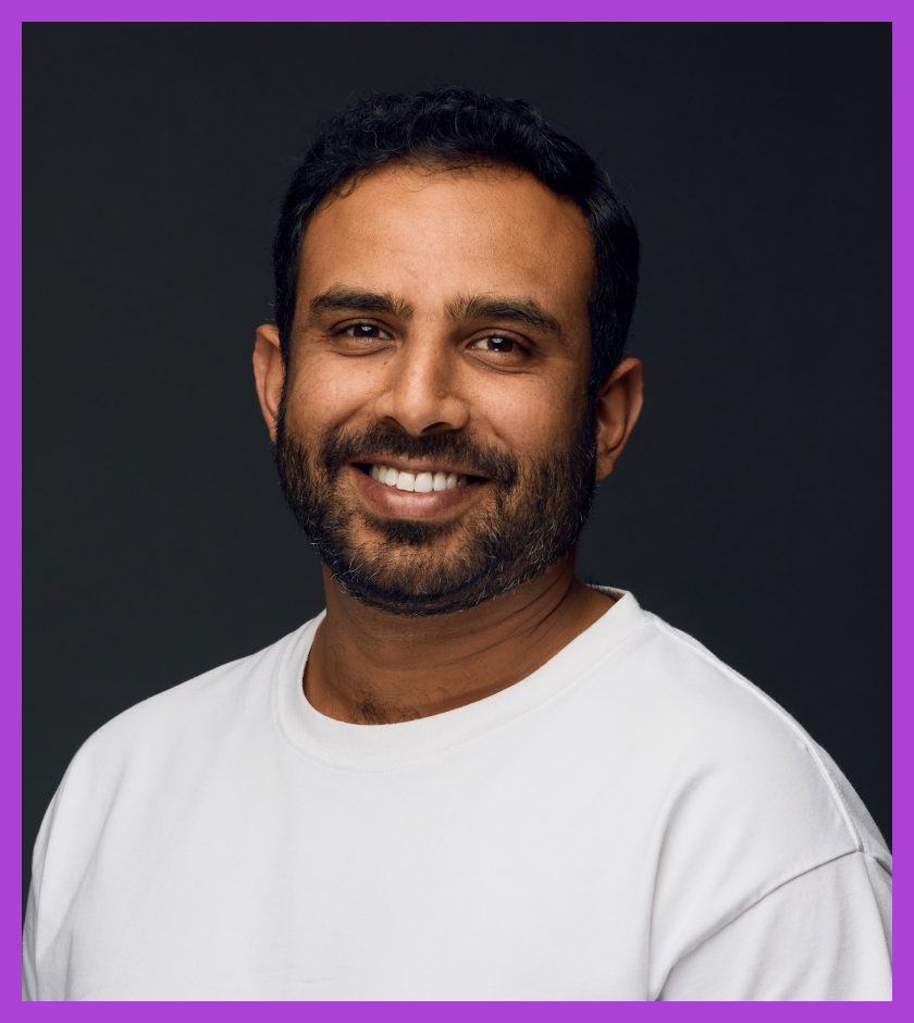Dipin is a middle-aged Indian male with short dark hair and a beard. He is wearing a white t-shirt and smiling at the camera.