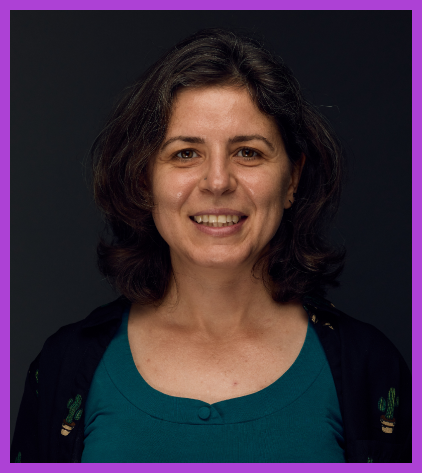 Lora is light skinned woman with light brown hair and wearing teal top and black cardigan, smiling at the camera.