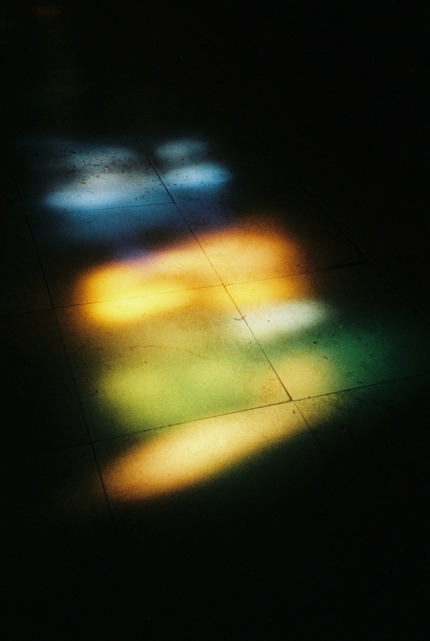 Colorful light reflections on a tiled floor in darkness.