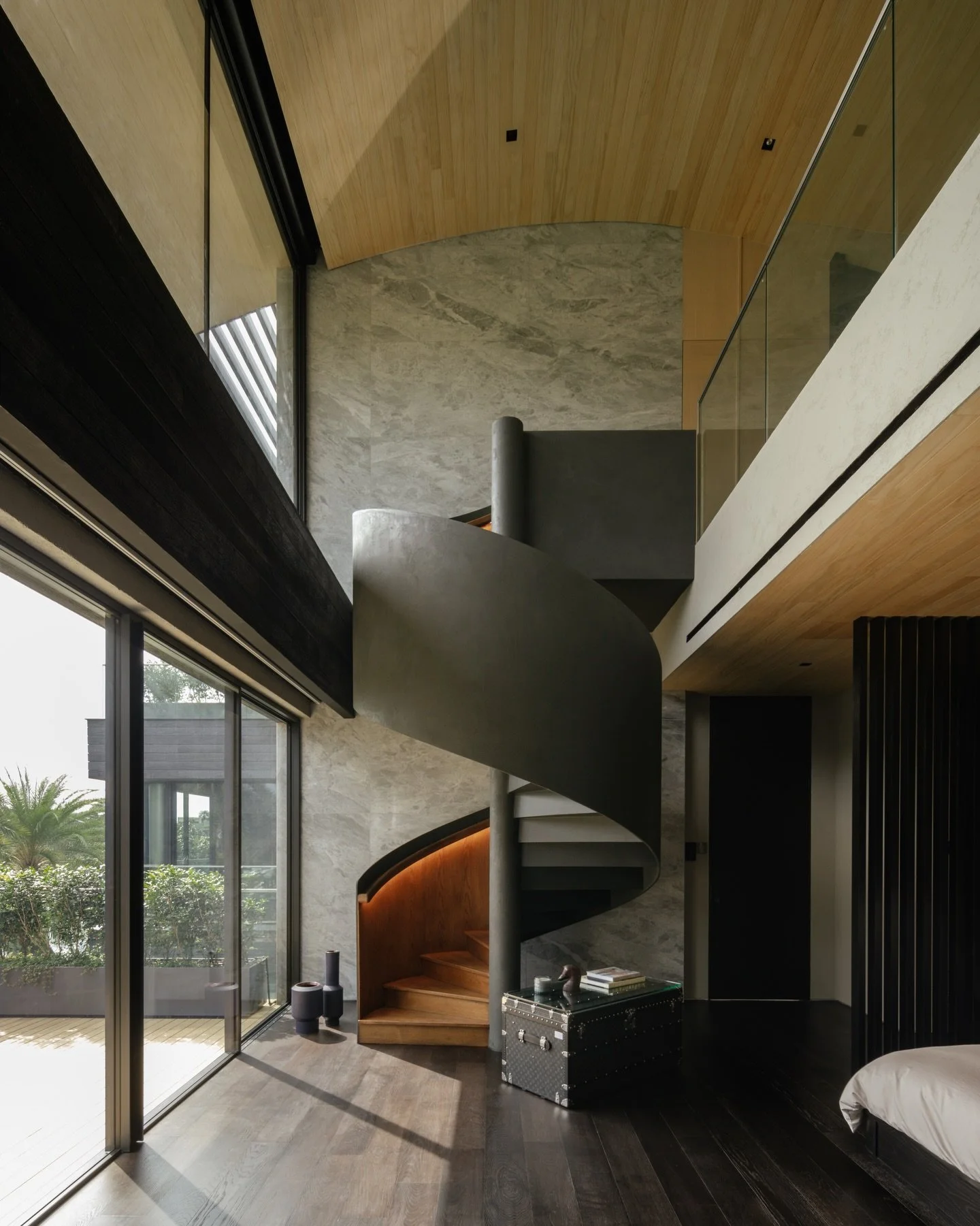 Within the master suite, a double-volume bedroom faces the waterway, framing expansive views across the landscape. The height of the space allows morning light to enter deeply into the room, gradually illuminating the mineral surfaces and timber fini