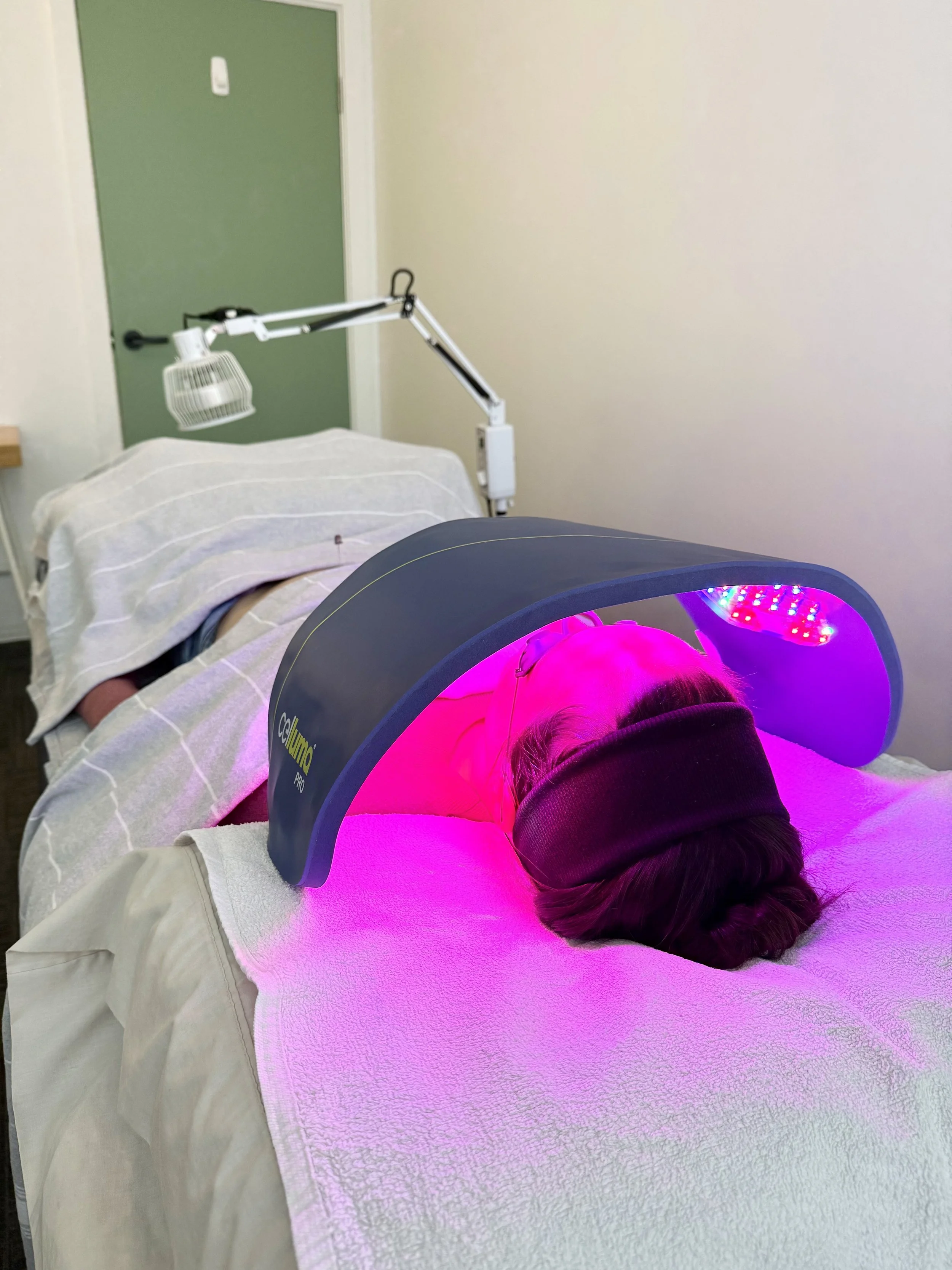 A woman having a facial skin treatment under purple LED lights at a skincare clinic.