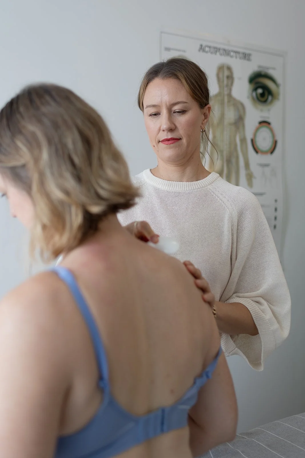 A healthcare professional performs a shoulder ultrasound on a patient in a medical setting, with a medical chart in the background.