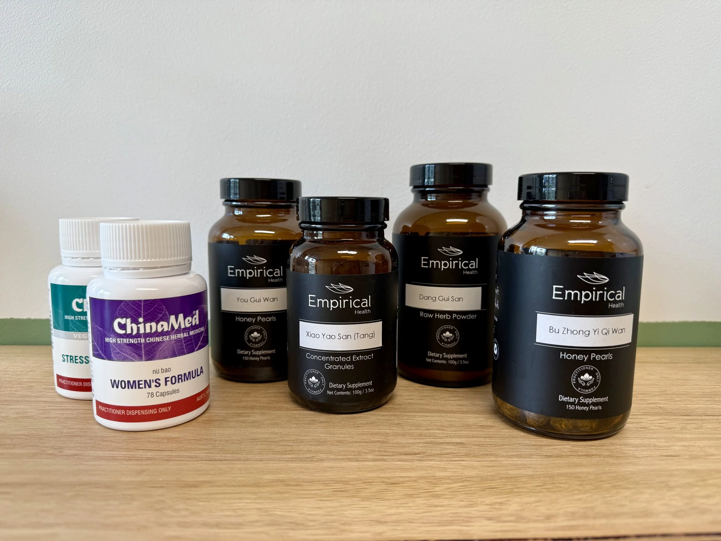 Assorted Chinese herbal medicine formulas on a wooden surface.