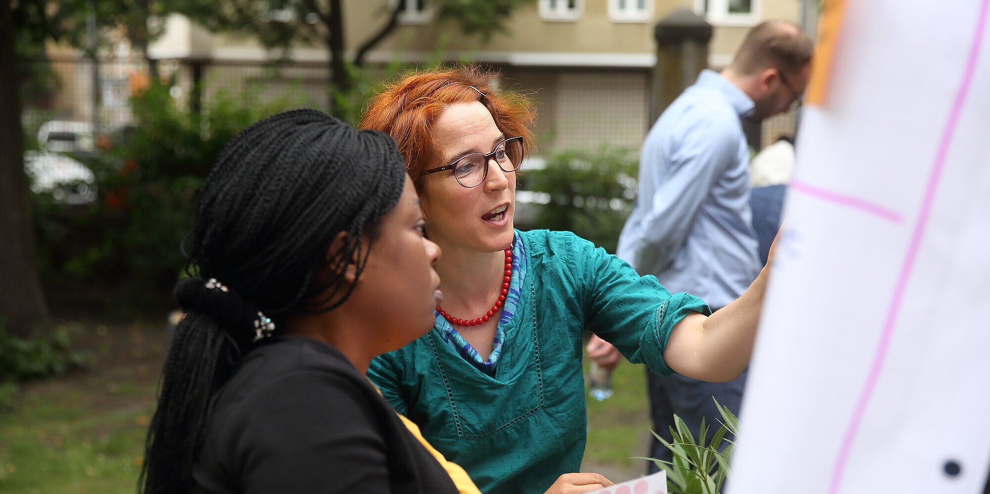 Zwei Frauen sprechen miteinander, während sie auf ein Flipchart blicken und gemeinsam daran arbeiten.
