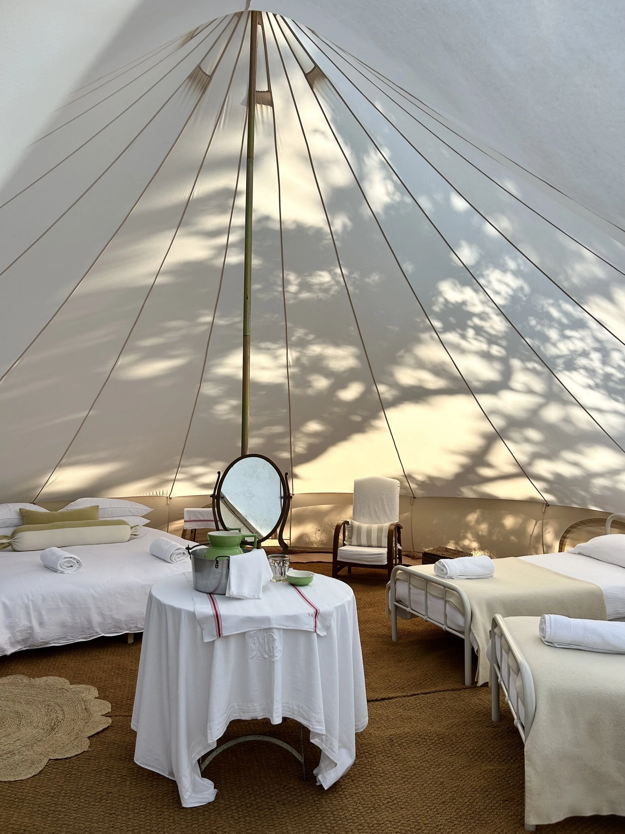 A luxury tent interior with beds, a mirror, and outdoor scenery visible through the tent wall.