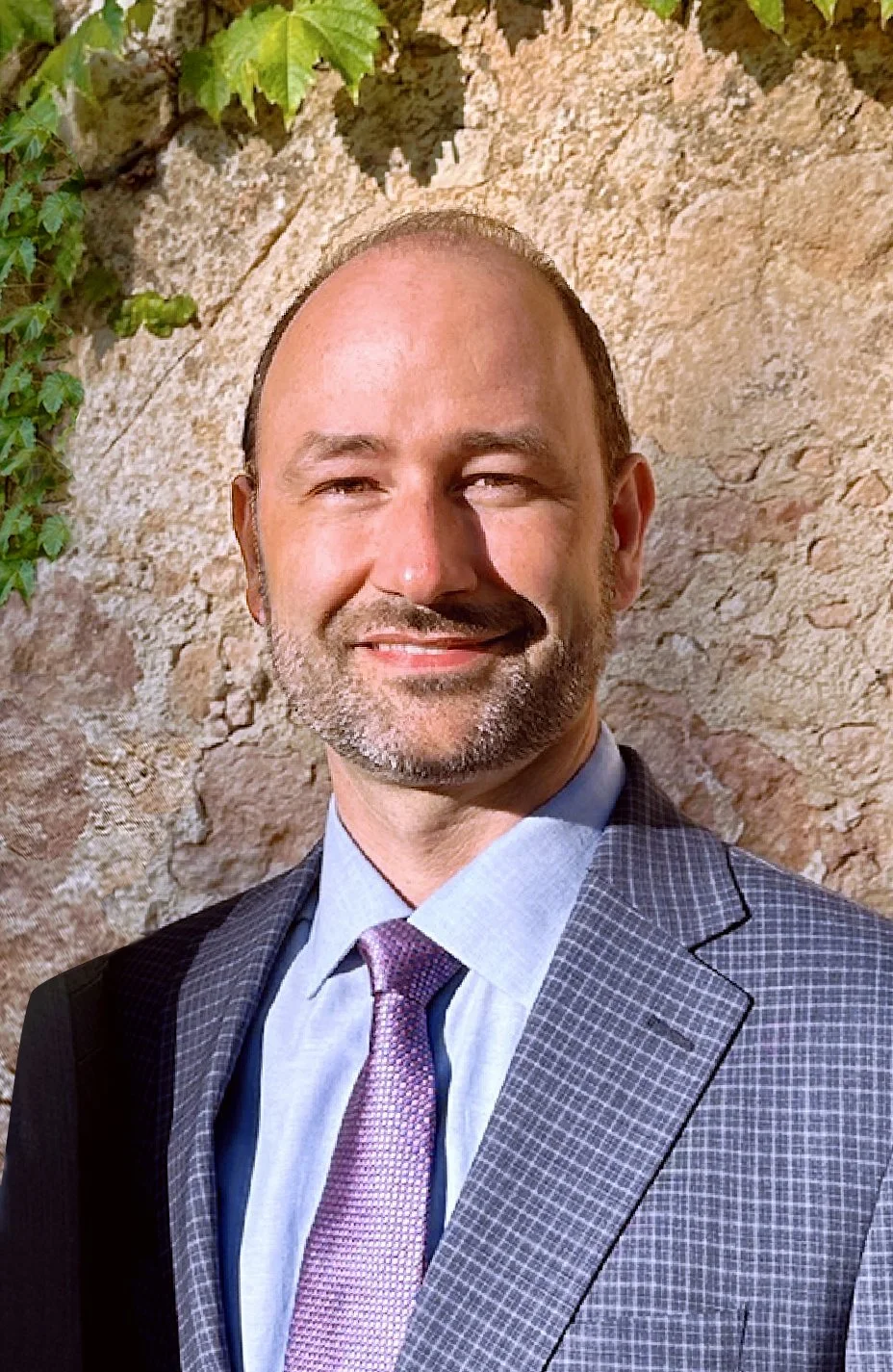 Smiling man in tuxedo standing in front of stone columns.