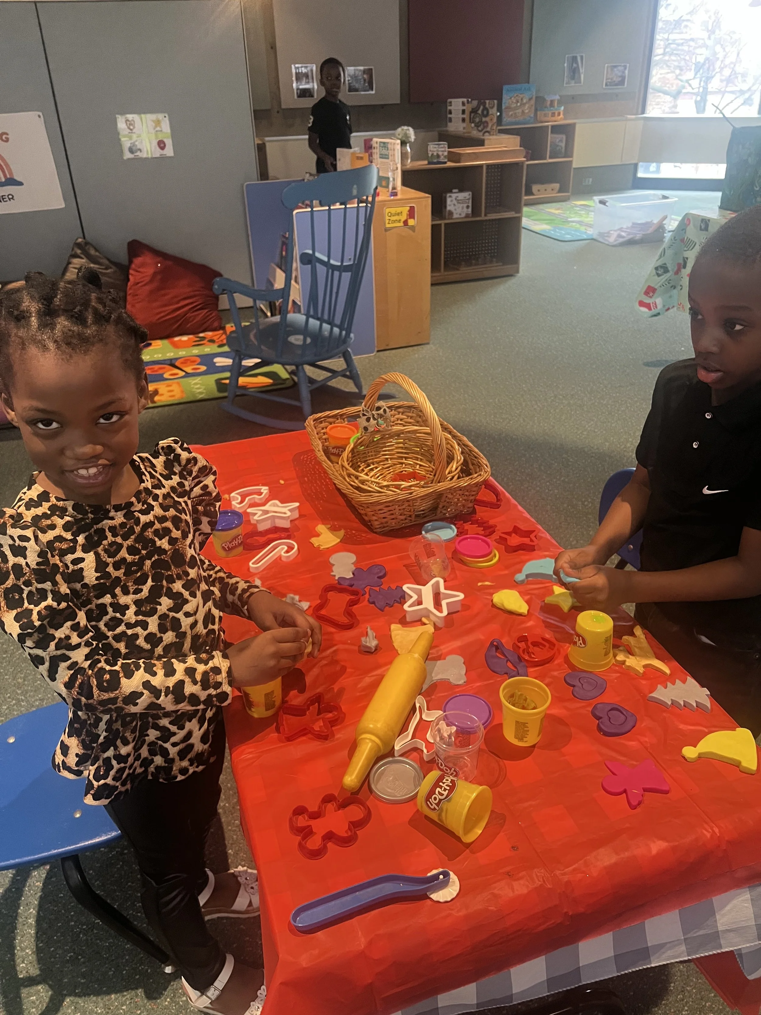 Children playing with Play-Doh and cookie cutters at a table in a classroom.