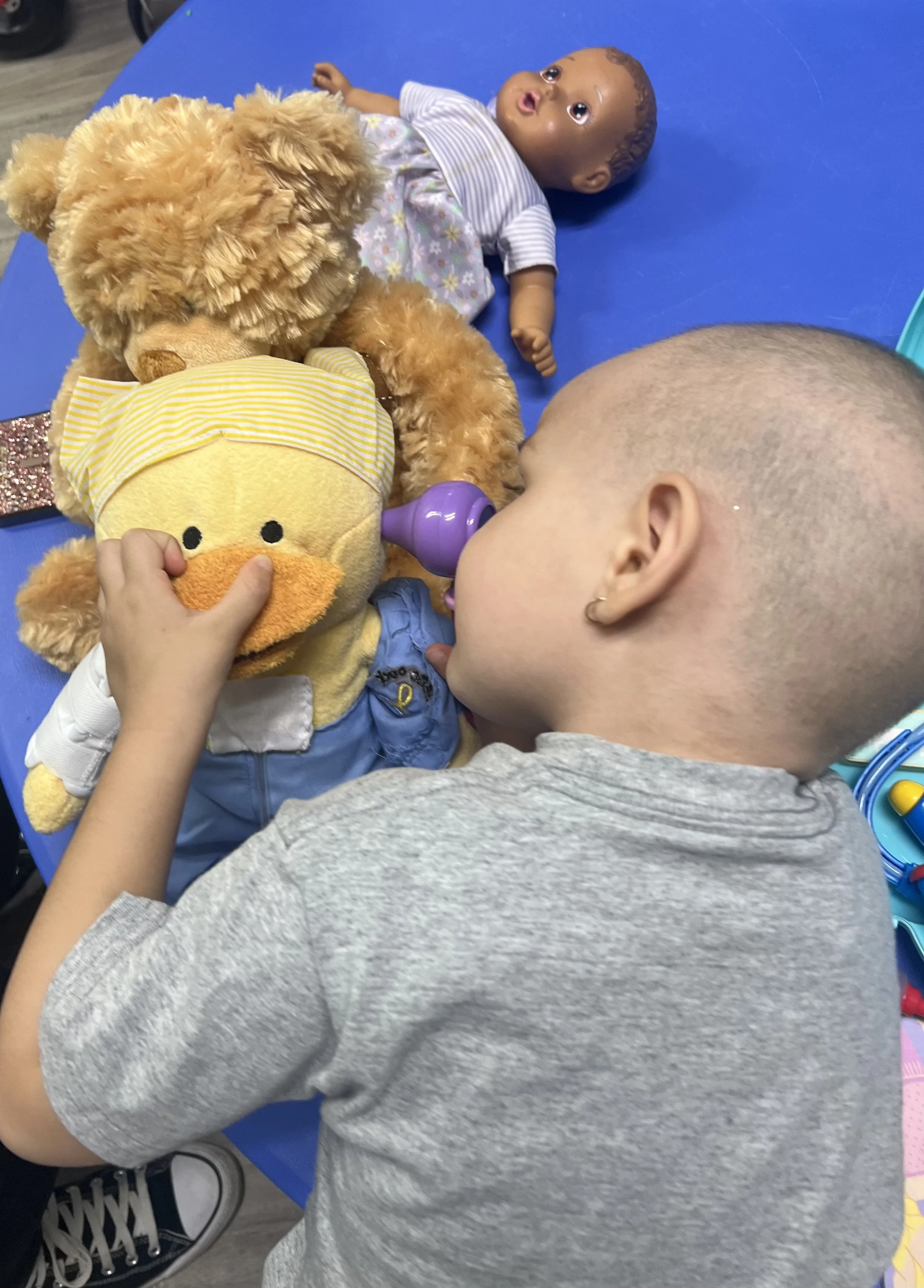 A young girl and a woman are sitting at a table, engaging in a painting activity. The girl is holding a paintbrush and the woman is overseeing her work.