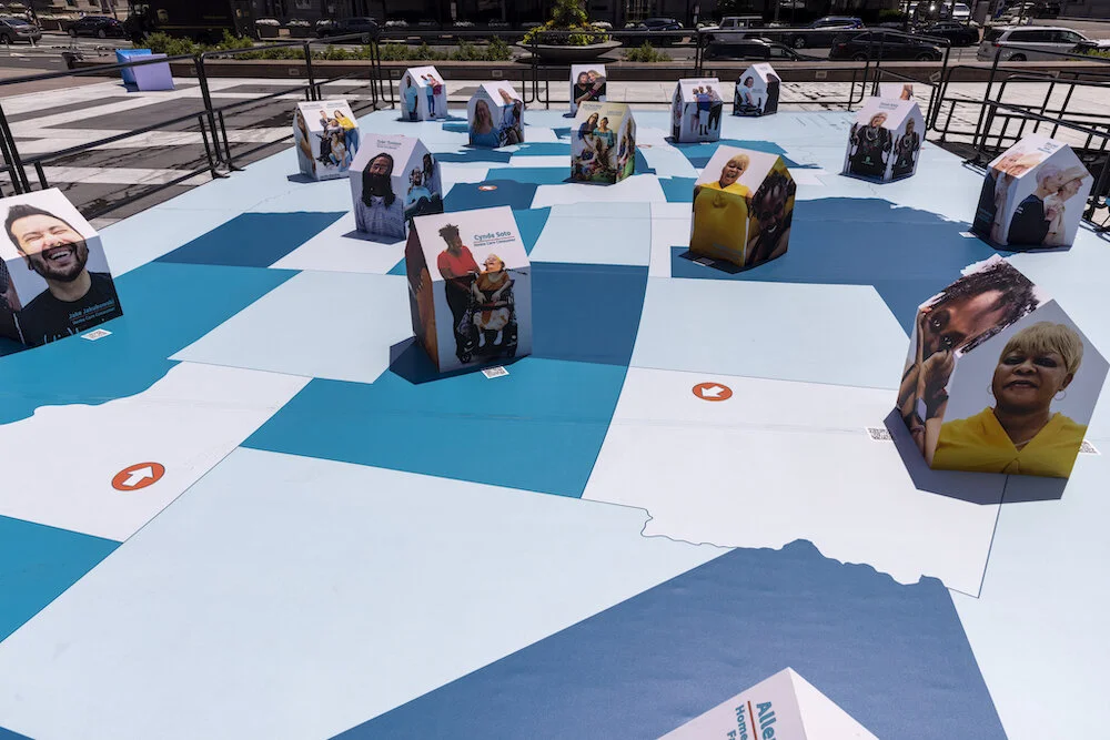 The Communities of Care Installation: Miniature houses with photos of family caregivers, care consumers, and care workers plastered on them are placed a cross a map of the United States.