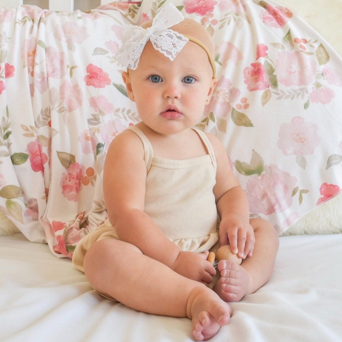 Baby girl sitting in front of Painted Petals super soft knit swaddle blanket with watercolor flowers in pale pink, rosy pink, and light green.