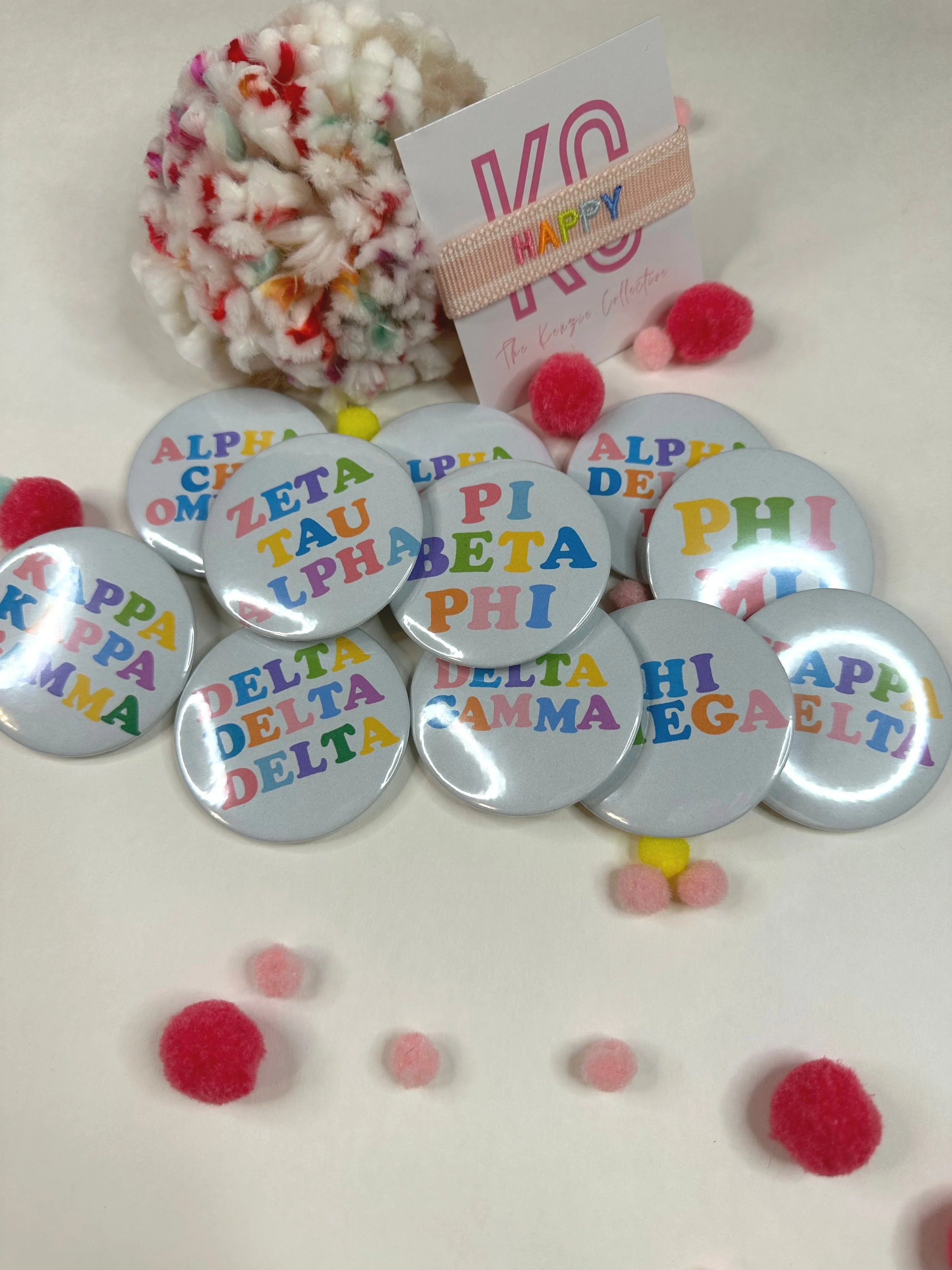 Eleven different colorful sorority buttons with their Greek names in bright colors piled up all together.