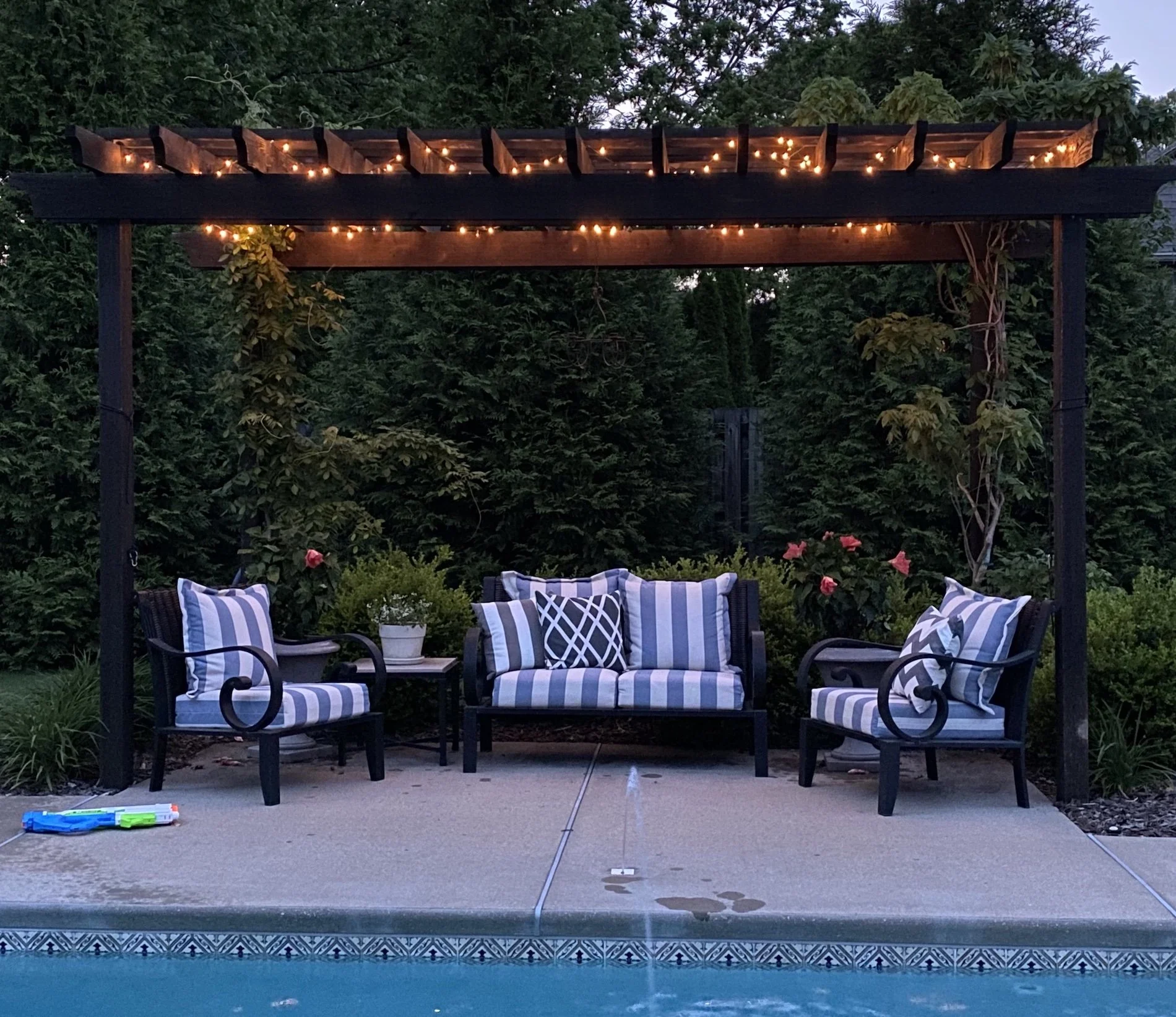 Outdoor pergola with twinkling lights and blue and white striped furniture.