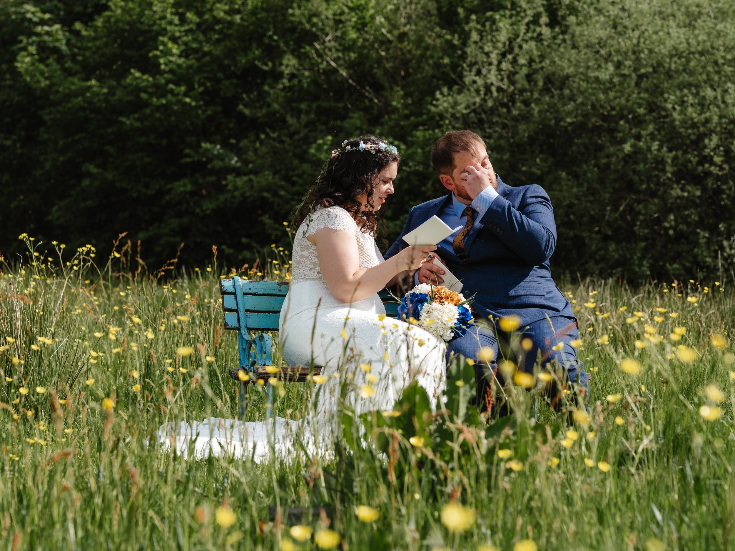 just married couple share vows privately in the meadow, the groom is crying while the bride reads her vows