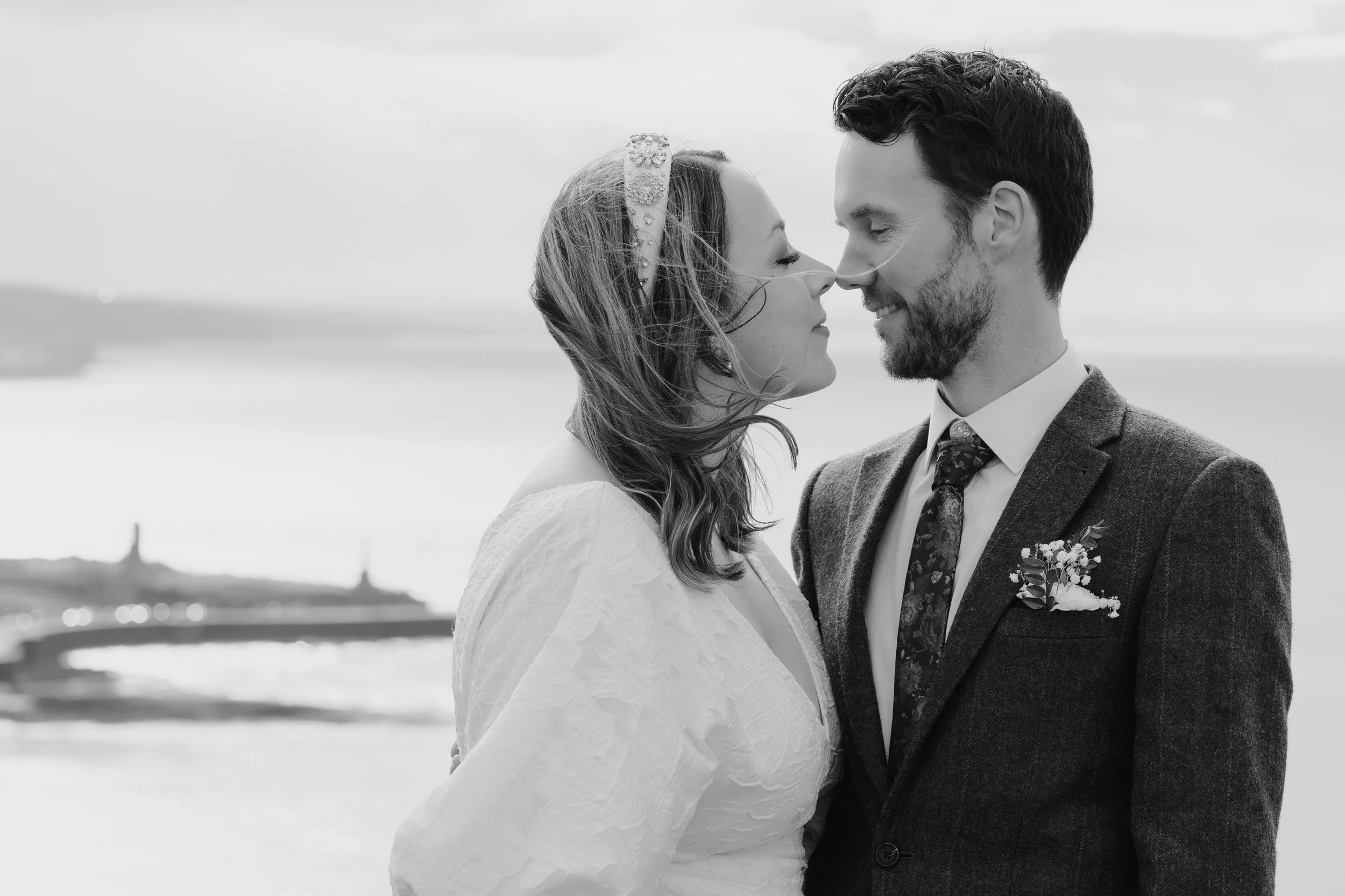 black & white bride & groom about to kiss, noses touching close up portrait with bokeh background of Aberystwyth pier