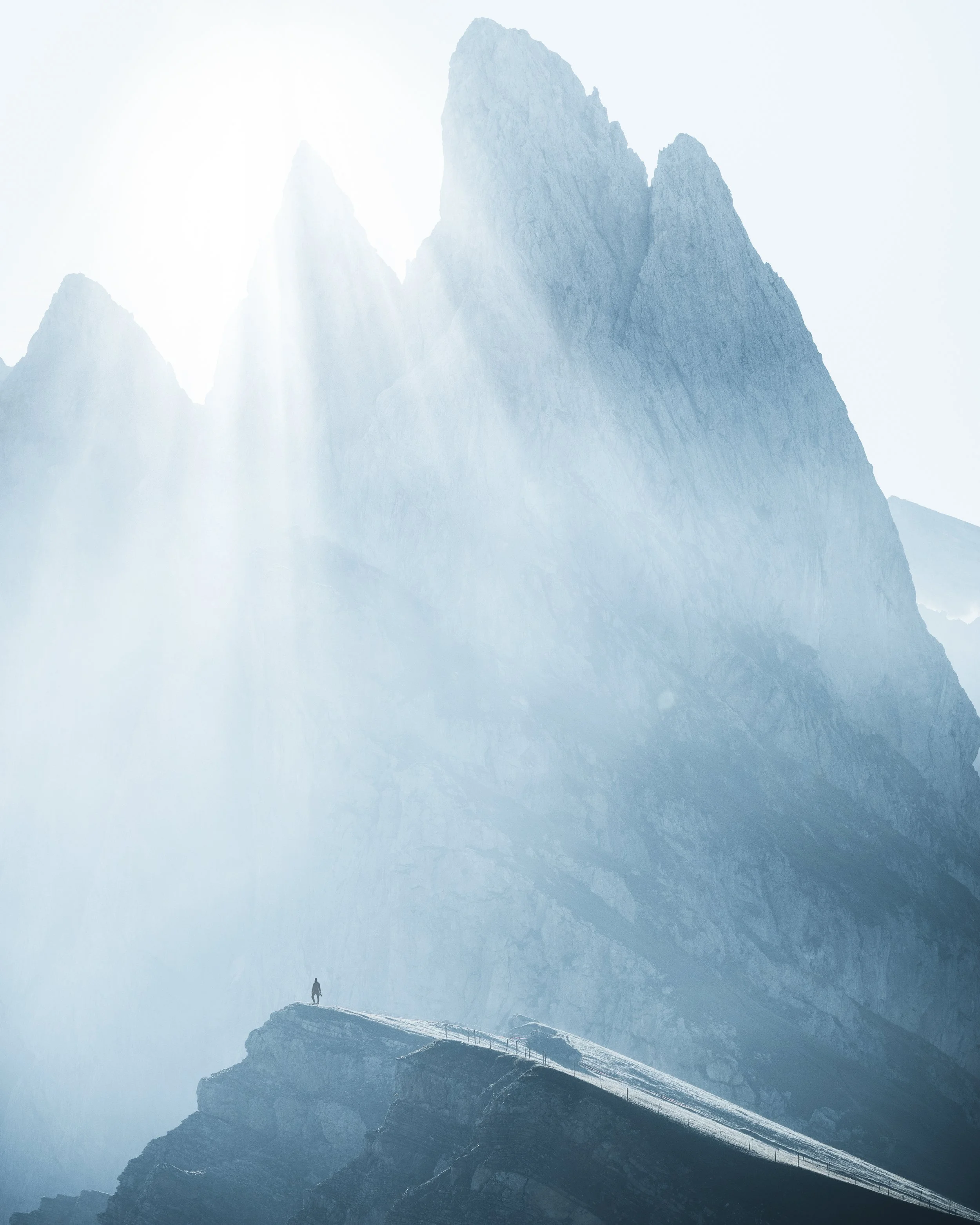 A hiker walking on a mountain ridge with towering peaks in the background, illuminated by soft sunlight.