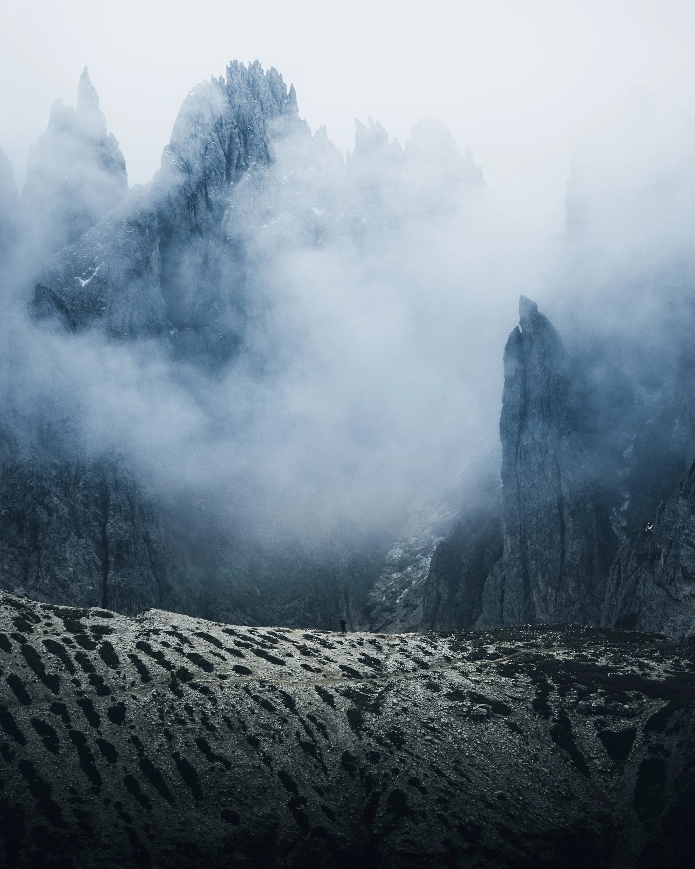 A foggy mountain landscape with towering jagged peaks and a small figure standing in the foreground.