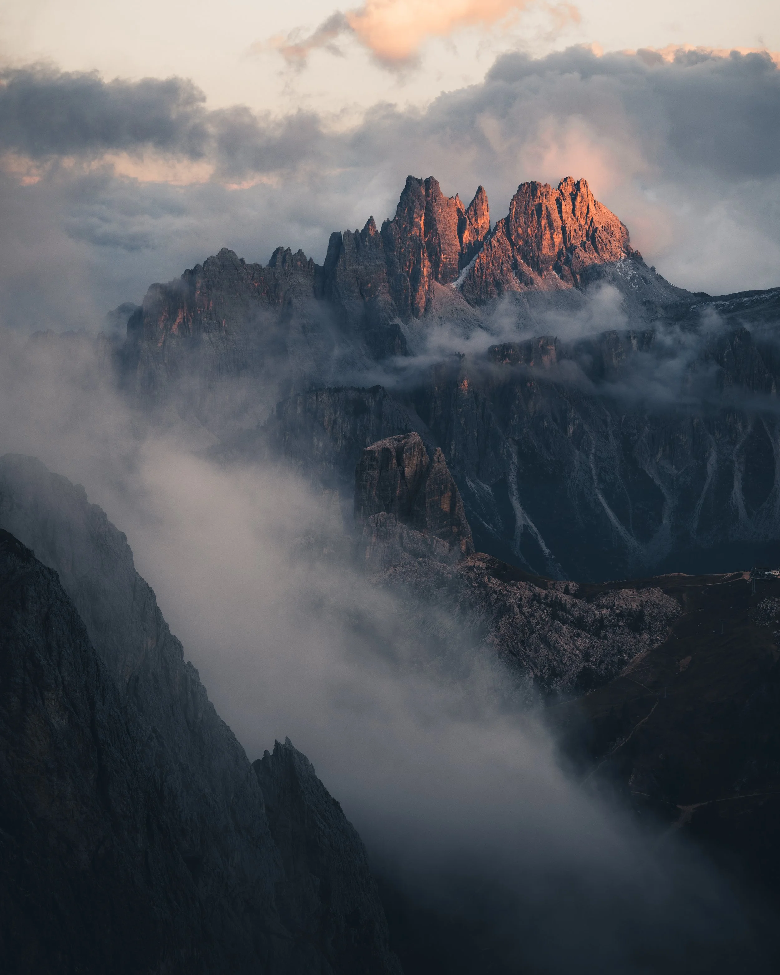 Mountain peaks illuminated by the setting sun, with clouds and mist surrounding the rugged terrain.