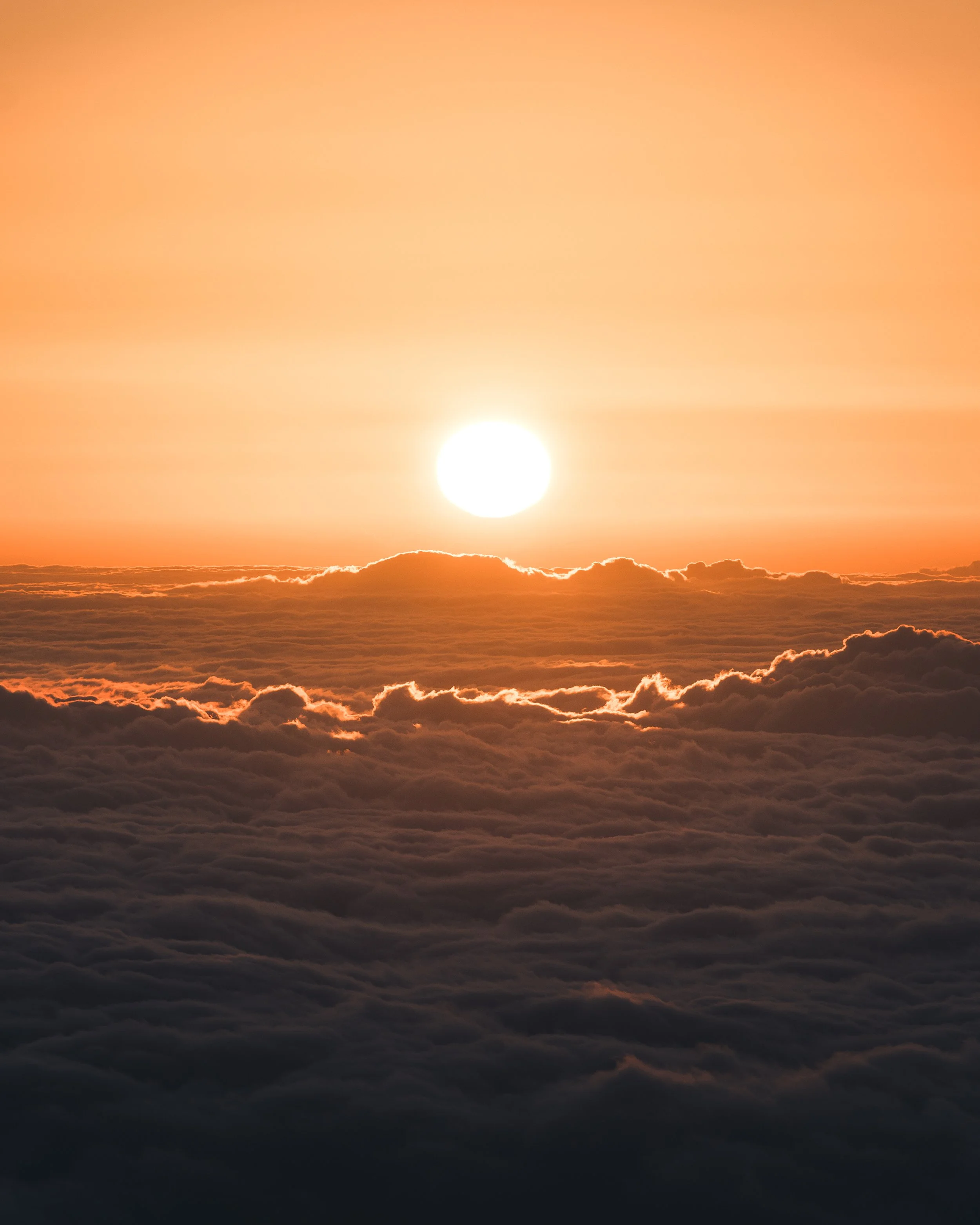 A sunset over a cloud-covered horizon with the sun near the bottom center and a gradient of light orange and pink in the sky.