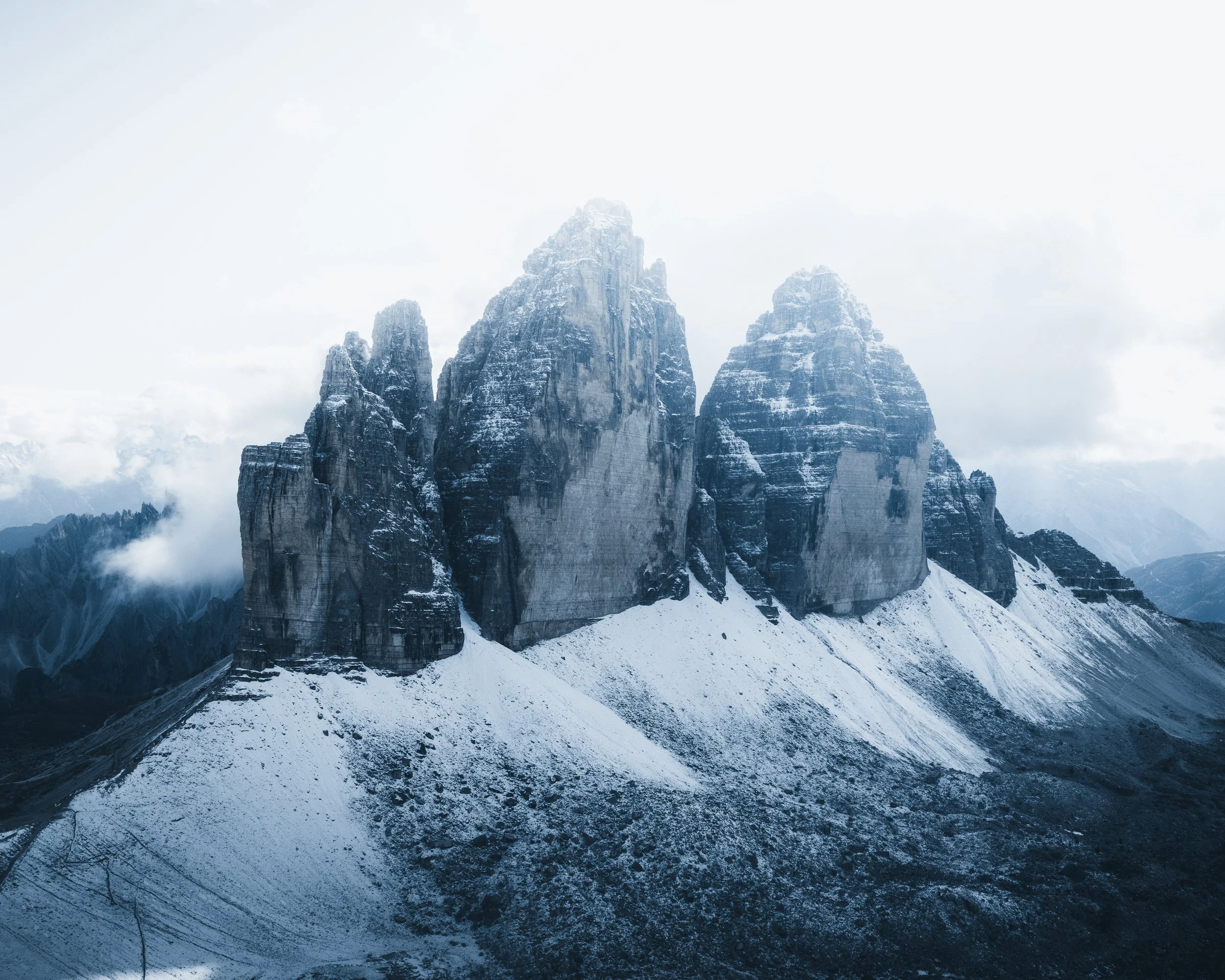 Snow-covered mountain peaks with clouds in the sky and snow on the ground.