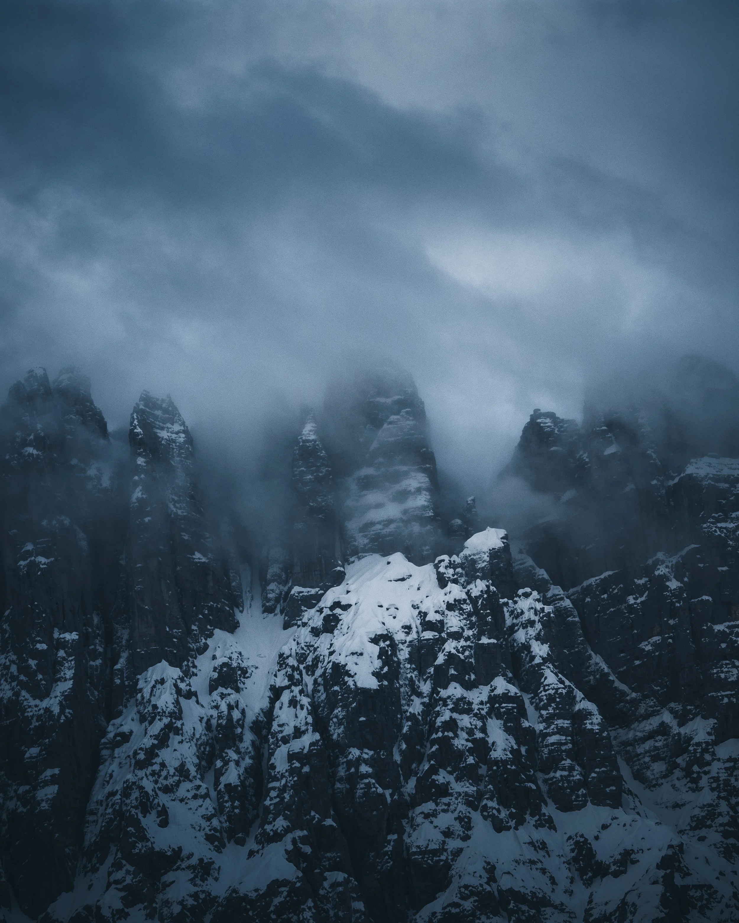 Snow-covered mountain peaks shrouded in fog, with a dark cloudy sky overhead.