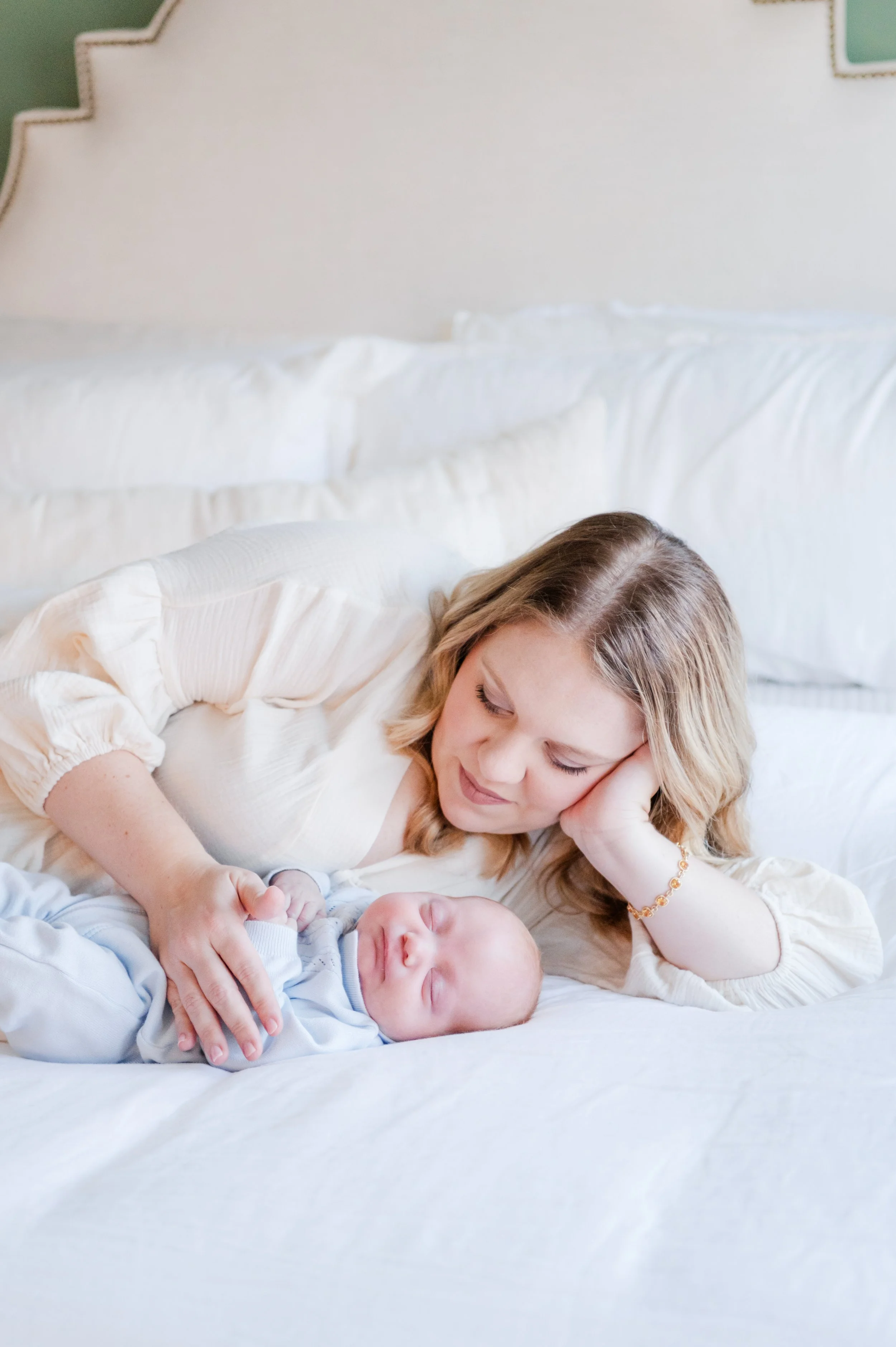 A Smyrna mom lying on a bed next to her sleeping baby, looking lovingly at the baby.