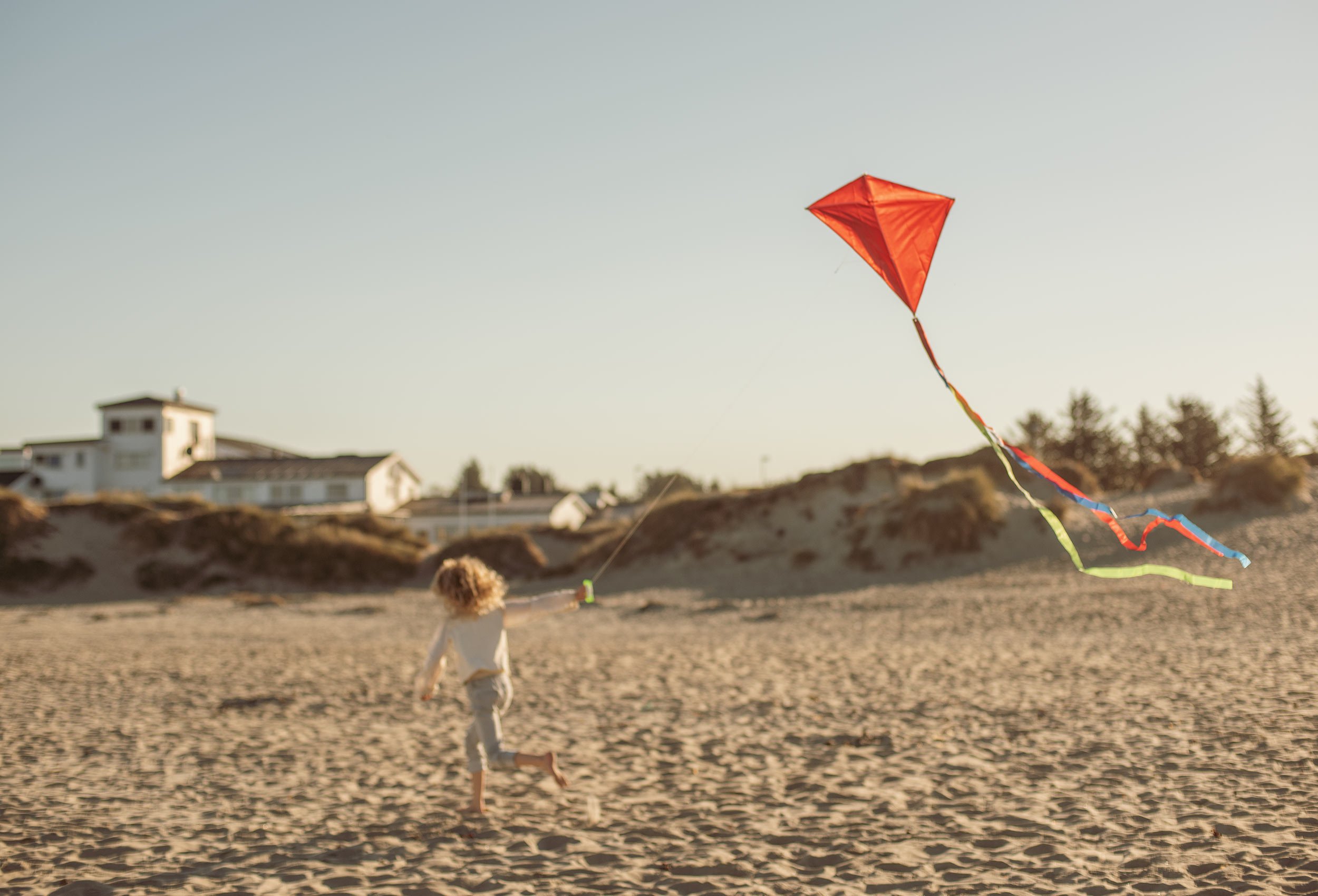 A child playing with a red kite in the wind on the beach at Sola Strand Hotel and Spa