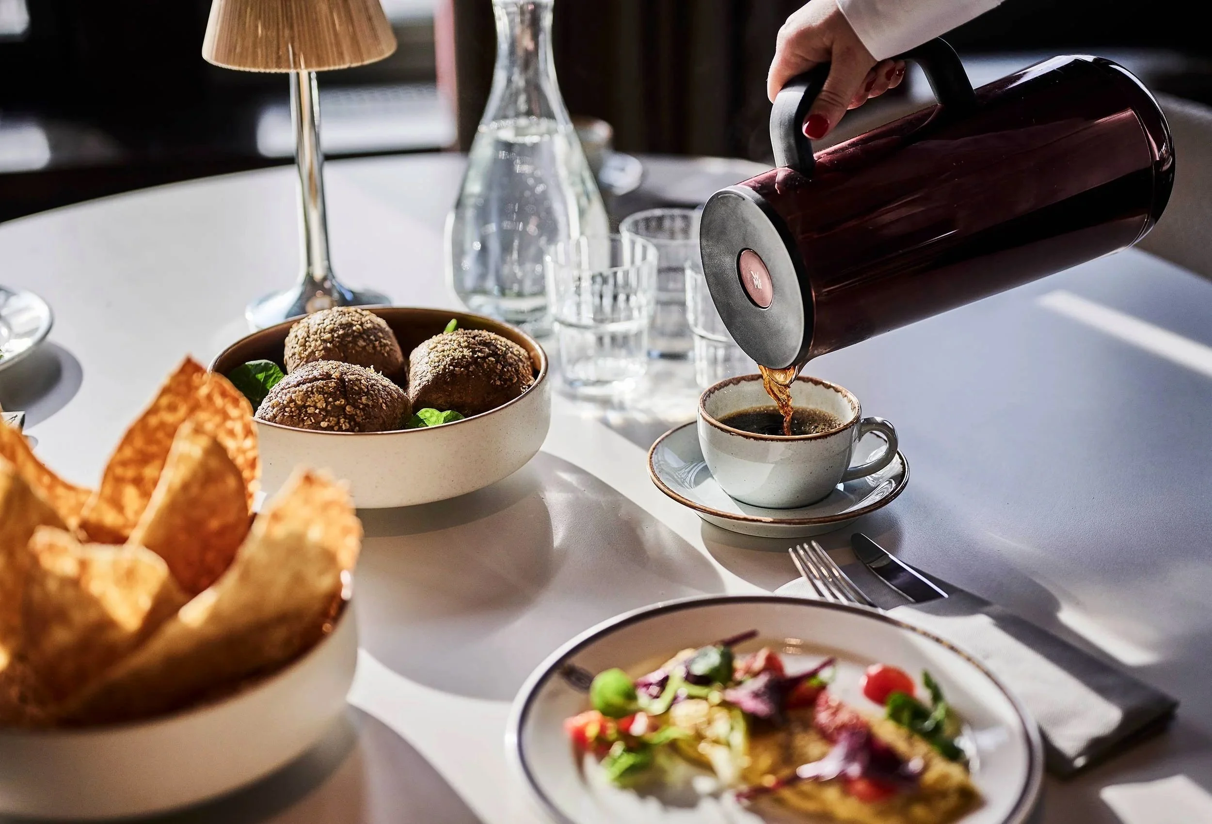 Mood picture from a dinner table with fresh hot coffee that is poured into the cup and good food on the table