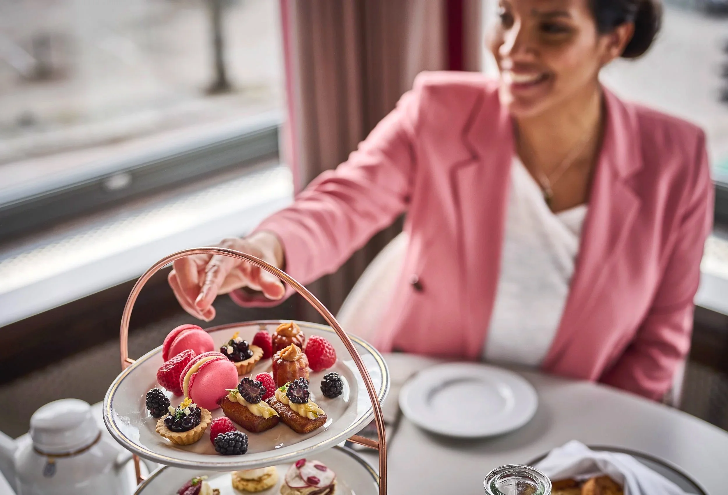 woman smiling and tasting dessert from appealing multi-tiered cake plate with macaroons, fresh berries and cookies in restaurant at Hotel Klubben