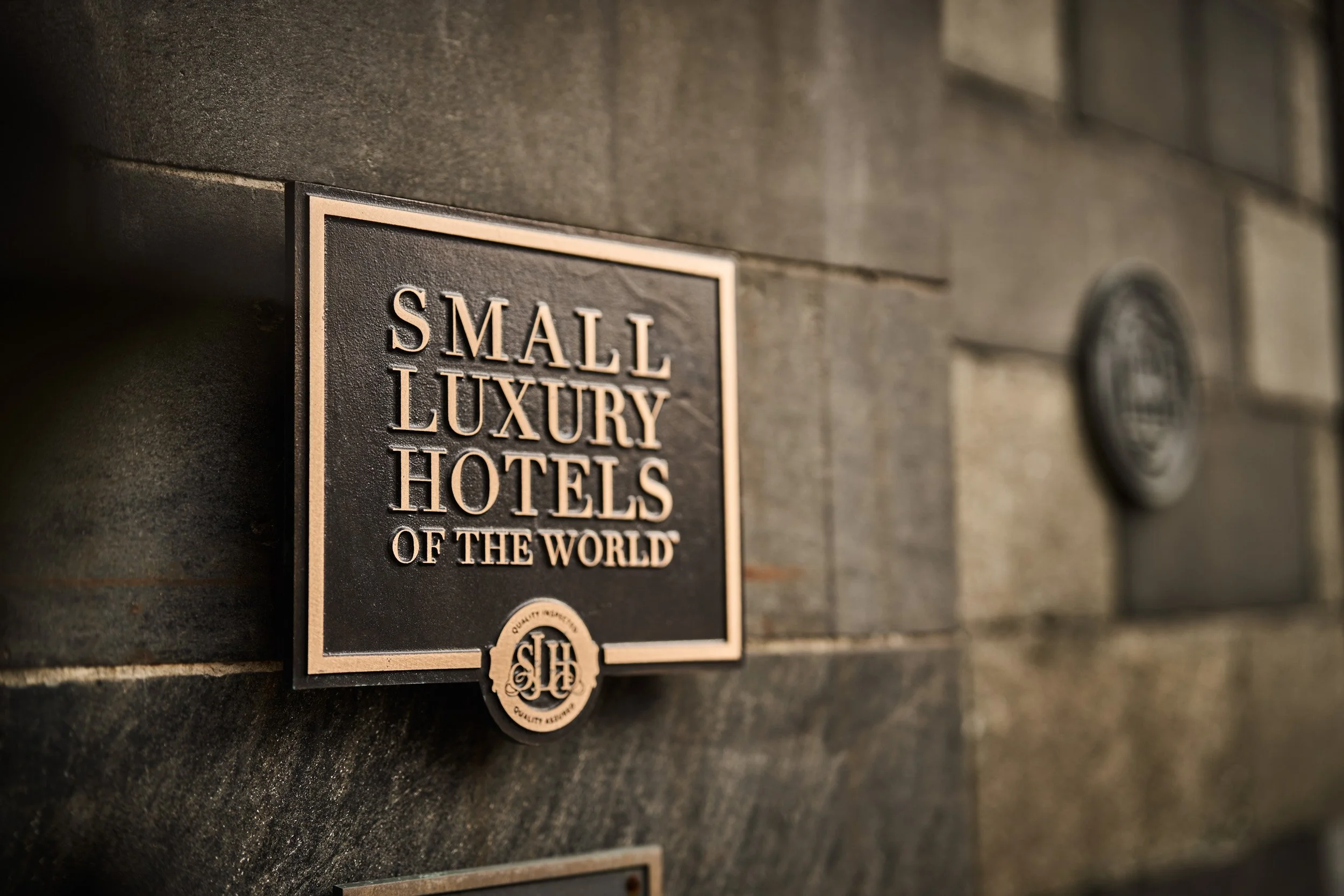 A black plaque on a stone wall reads 'Small Luxury Hotels of the World' with a gold emblem below.