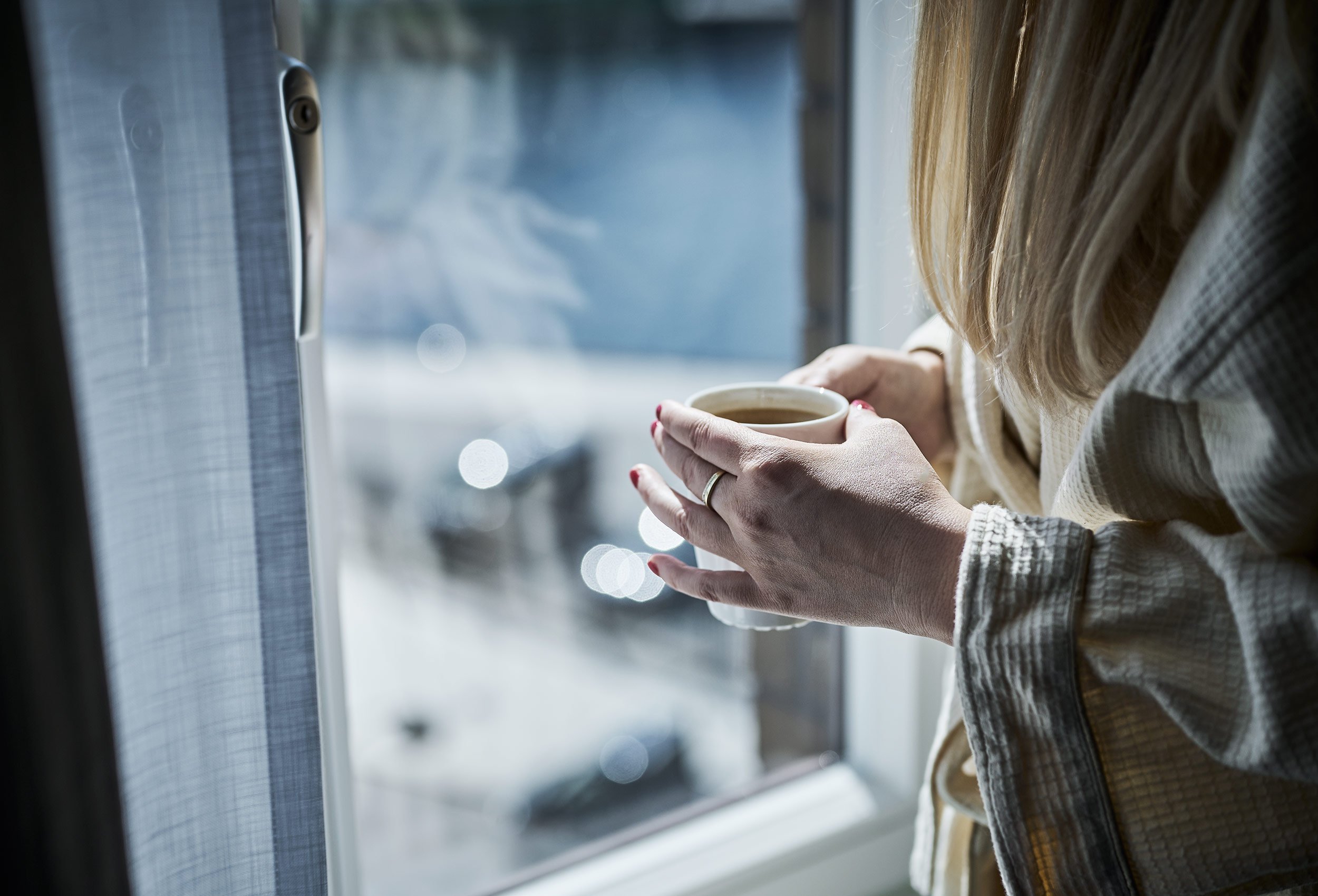 Woman in bath robe with fresh coffe looking out window in hotel suite Hotel victoria