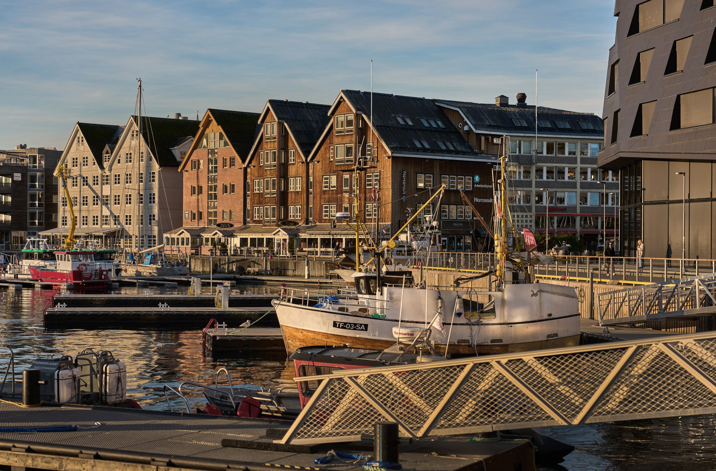 Boats docked at a harbor with traditional wooden waterfront buildings in the background during sunset.