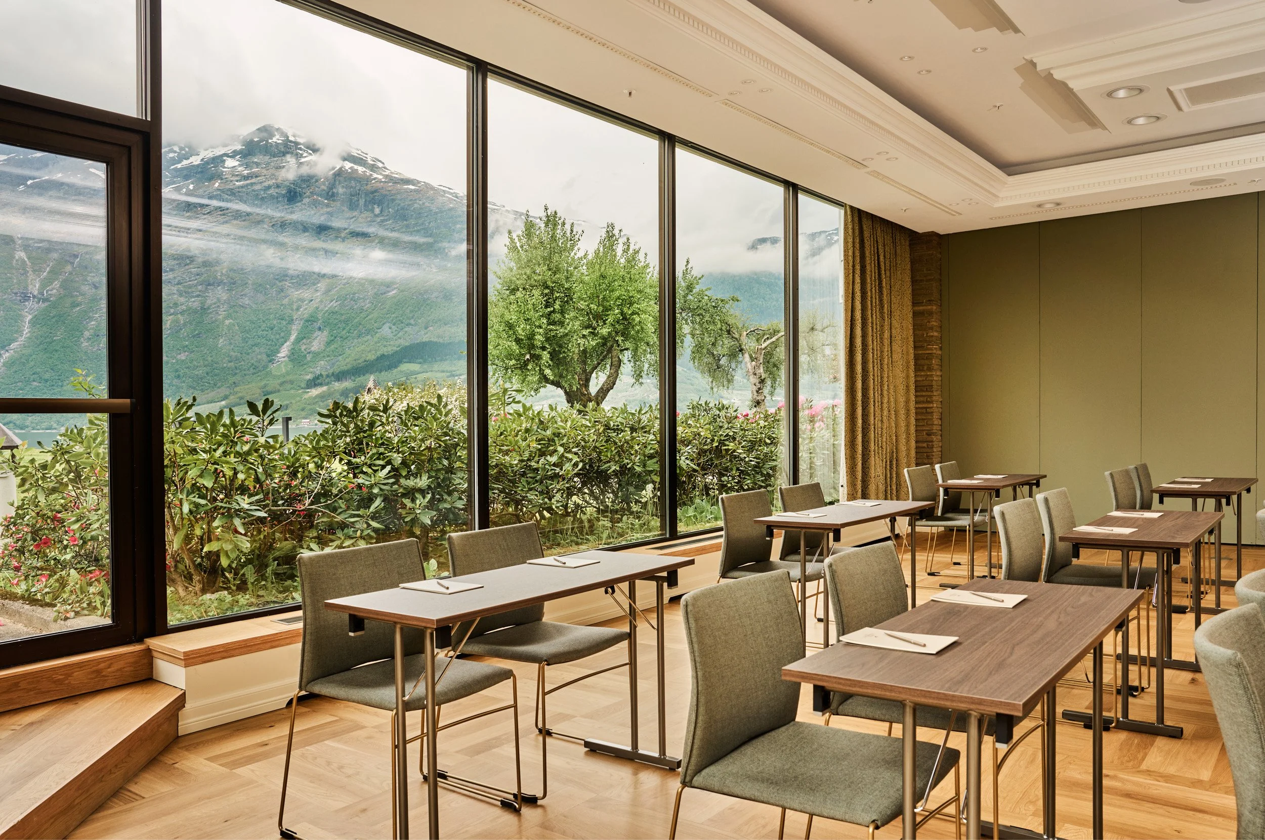 Empty conference room with tables and chairs facing large windows with mountain and greenery view.