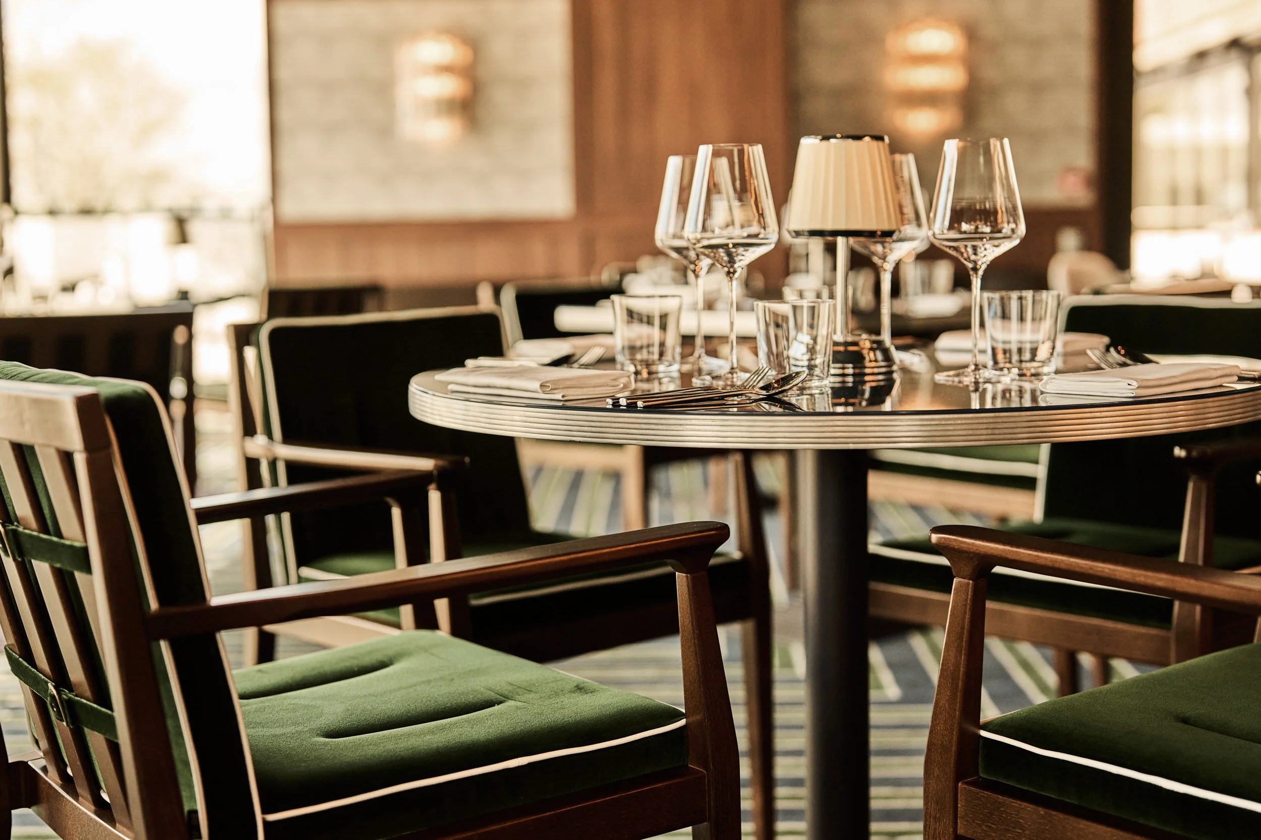 Upscale restaurant dining table set with wine glasses, water glasses, napkins, and cutlery in a well-lit, modern interior with wooden accents.