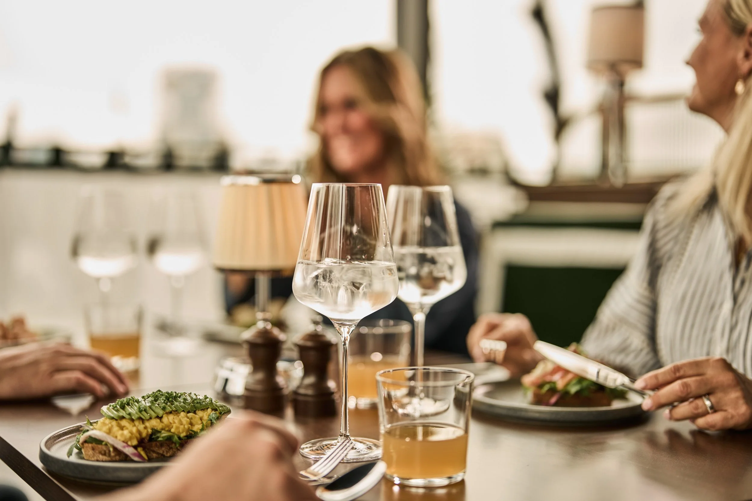 People dining at a restaurant with plates of food, glasses of water and beer, and salt and pepper shakers on the table.