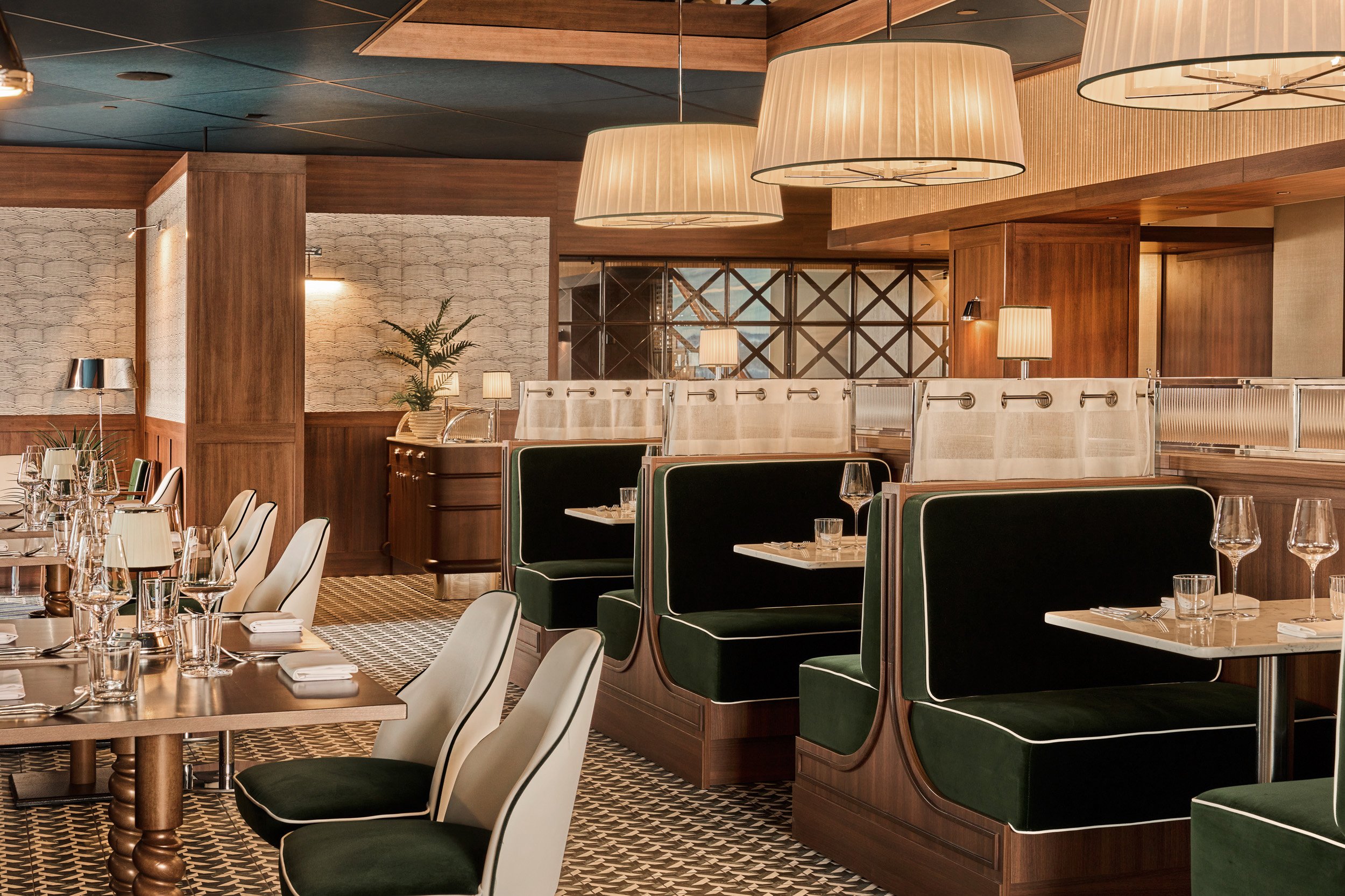 Interior of a fancy restaurant with wooden paneling, green upholstered booths, white chairs, and large hanging lamps, set for dining.