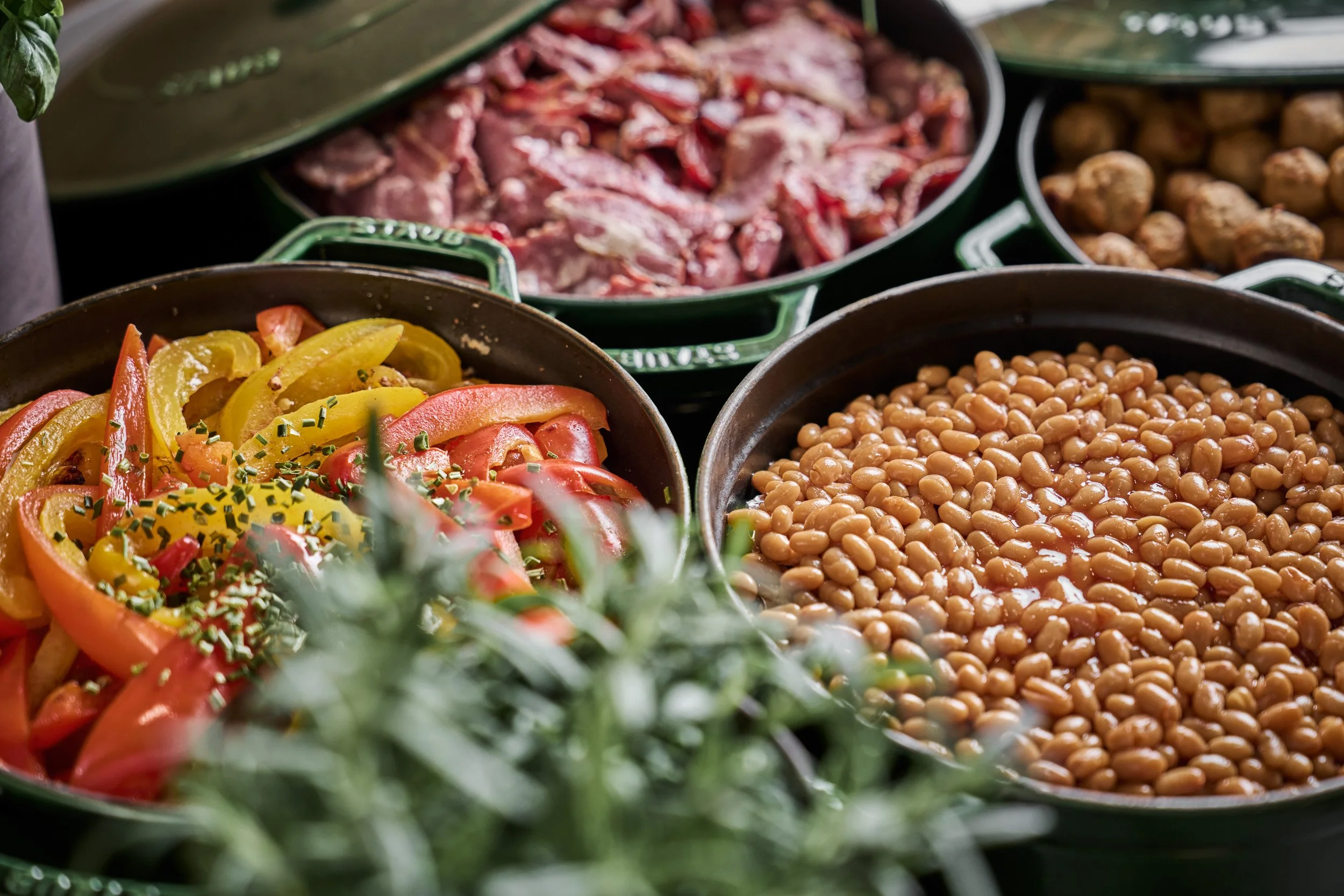 Assorted dishes including baked beans, sliced tomatoes and peppers, raw meat, and potatoes in serving bowls.